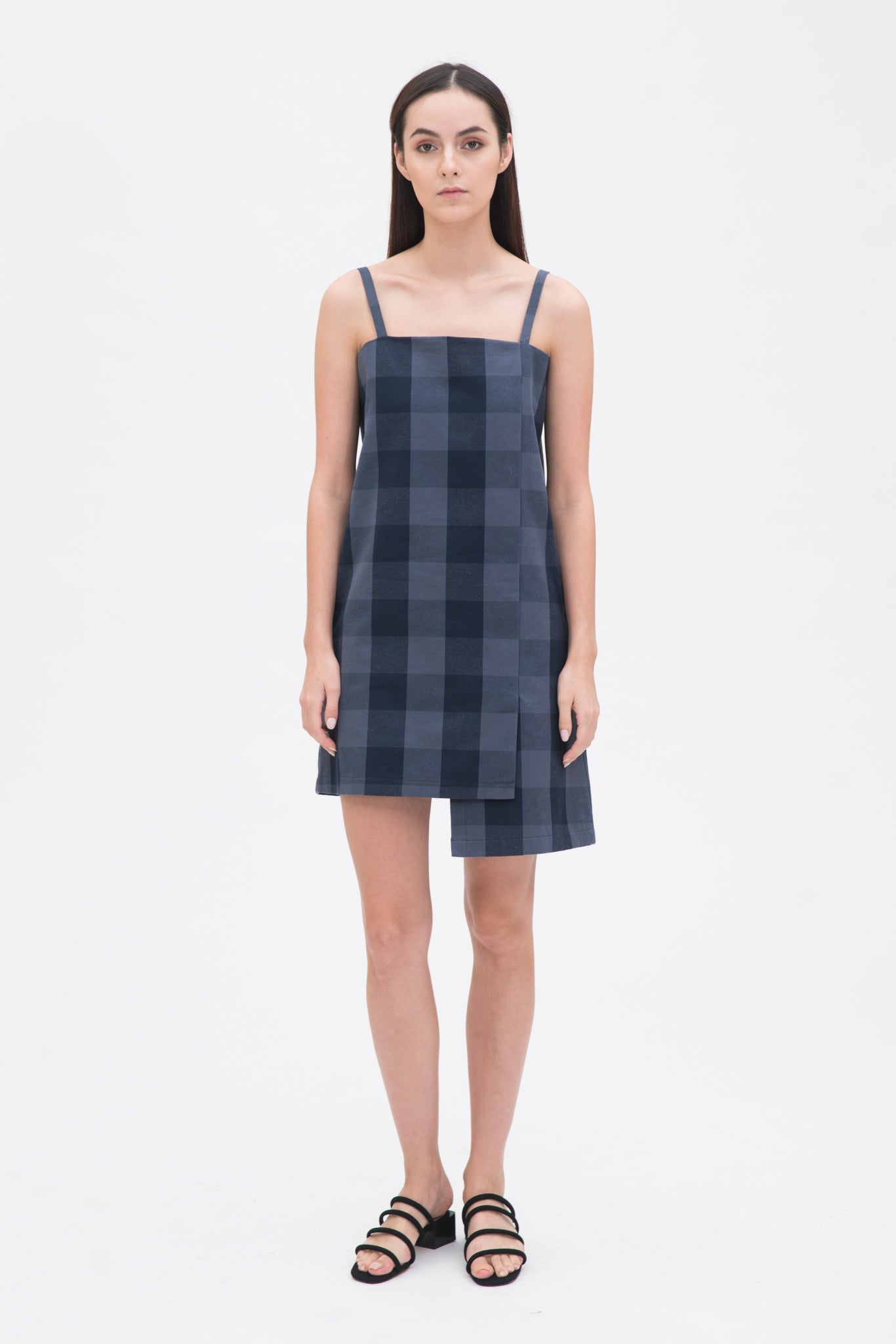 A woman with long dark hair is wearing a navy check dress and  black sandals