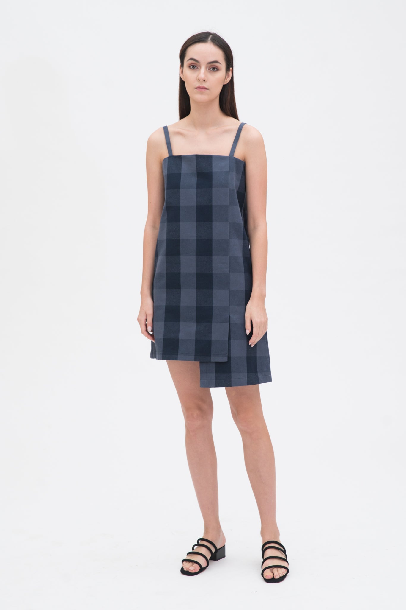 A woman with long dark hair is wearing a navy check dress and  black sandals