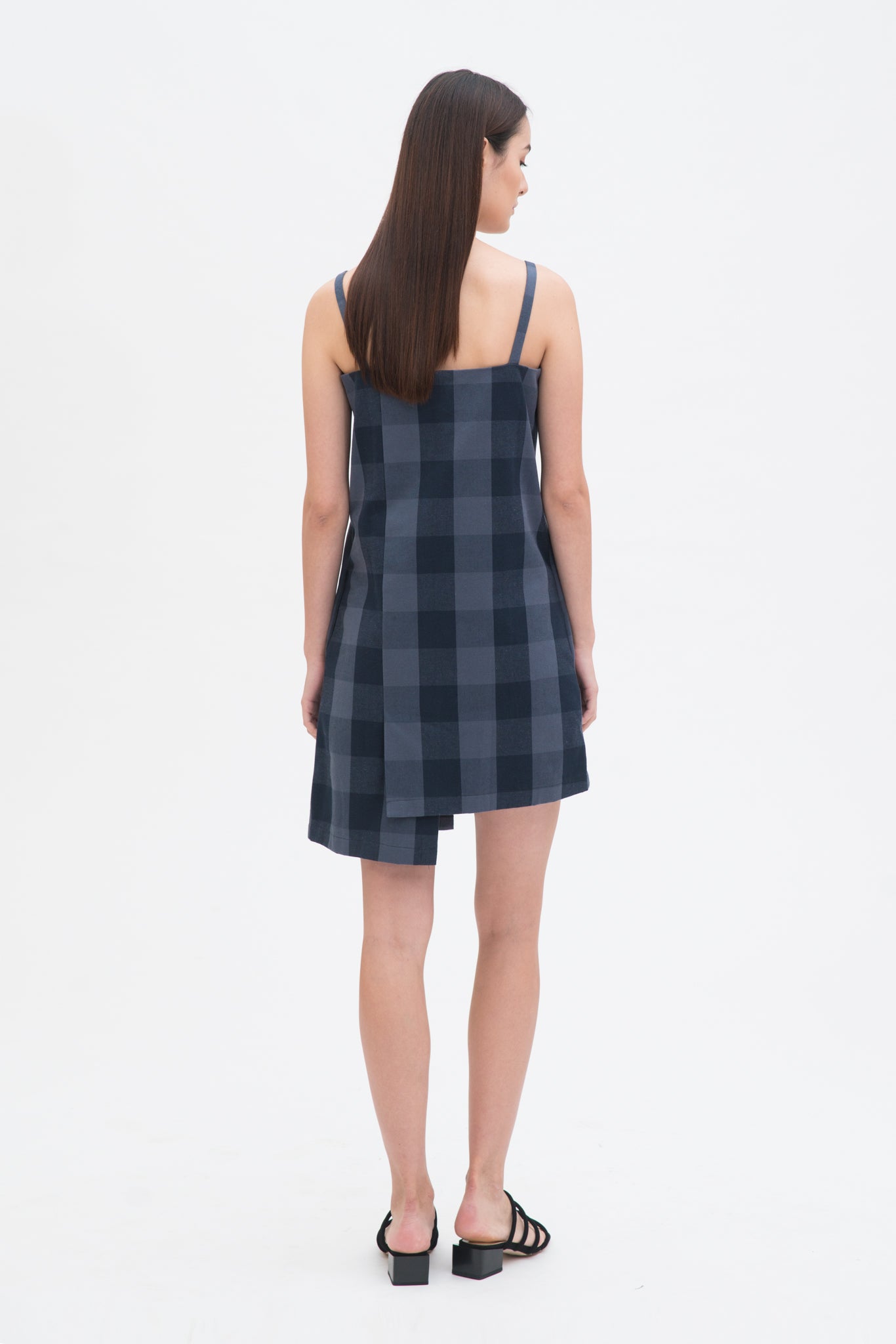 A woman with long dark hair is wearing a navy check dress  and  black sandals