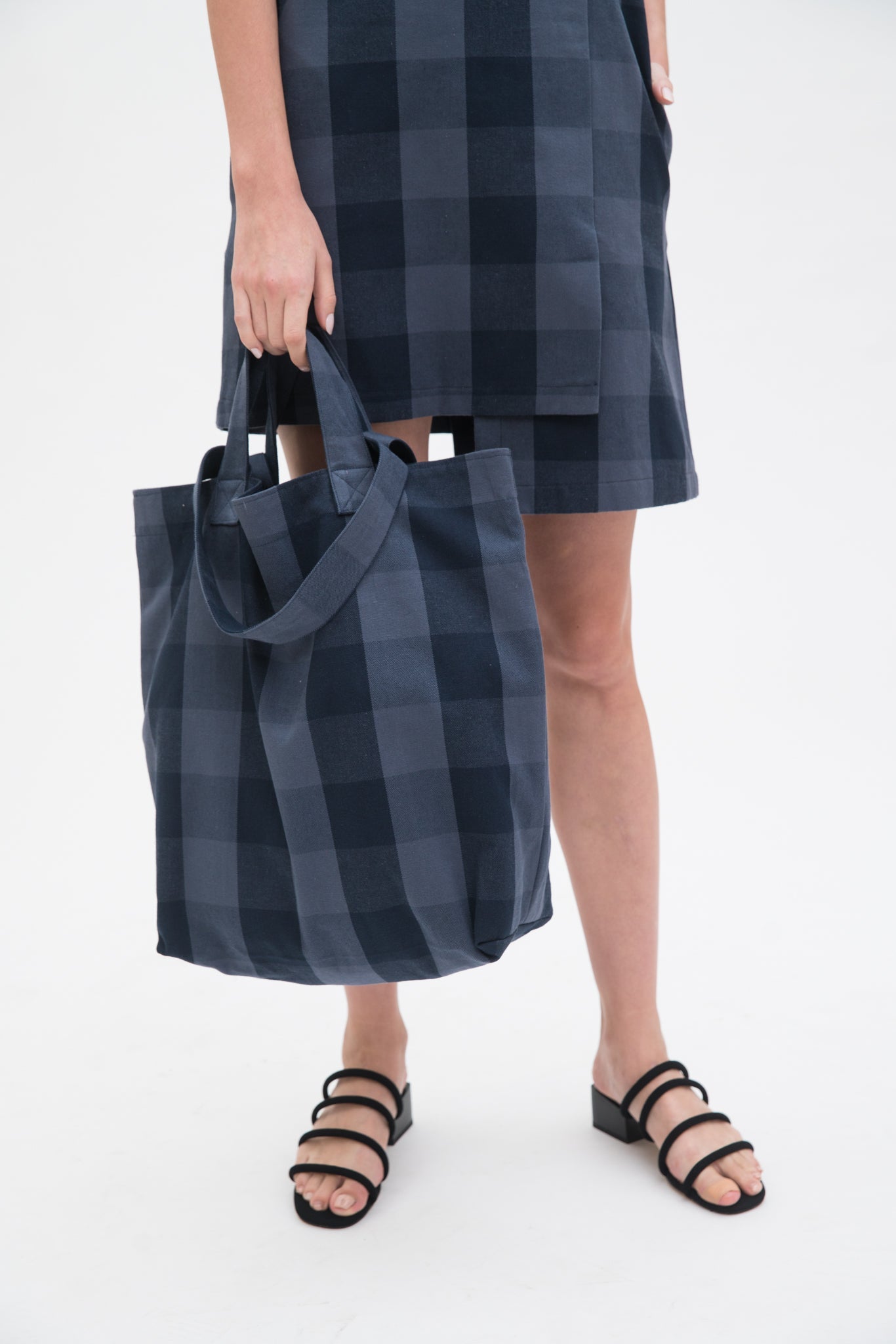A woman in a blue checked dress is holding a blue checked tote bag