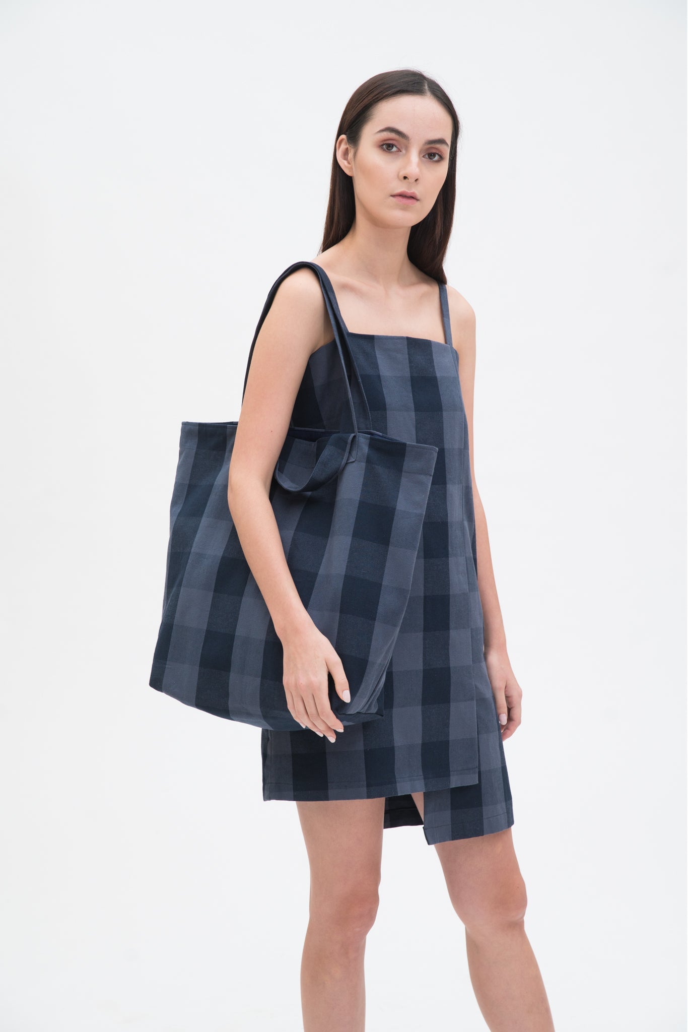 A woman in a blue checked dress is holding a blue checked tote bag