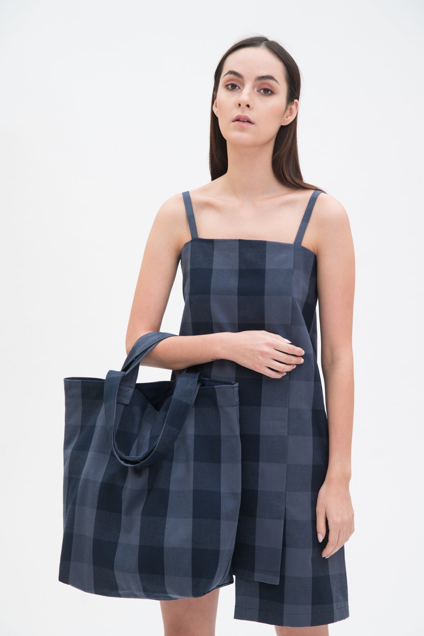 A woman in a blue checked dress is holding a blue checked tote bag