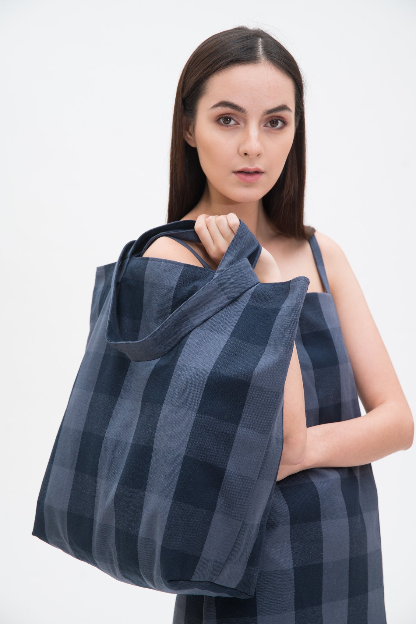A woman in a blue checked dress is holding a blue checked tote bag