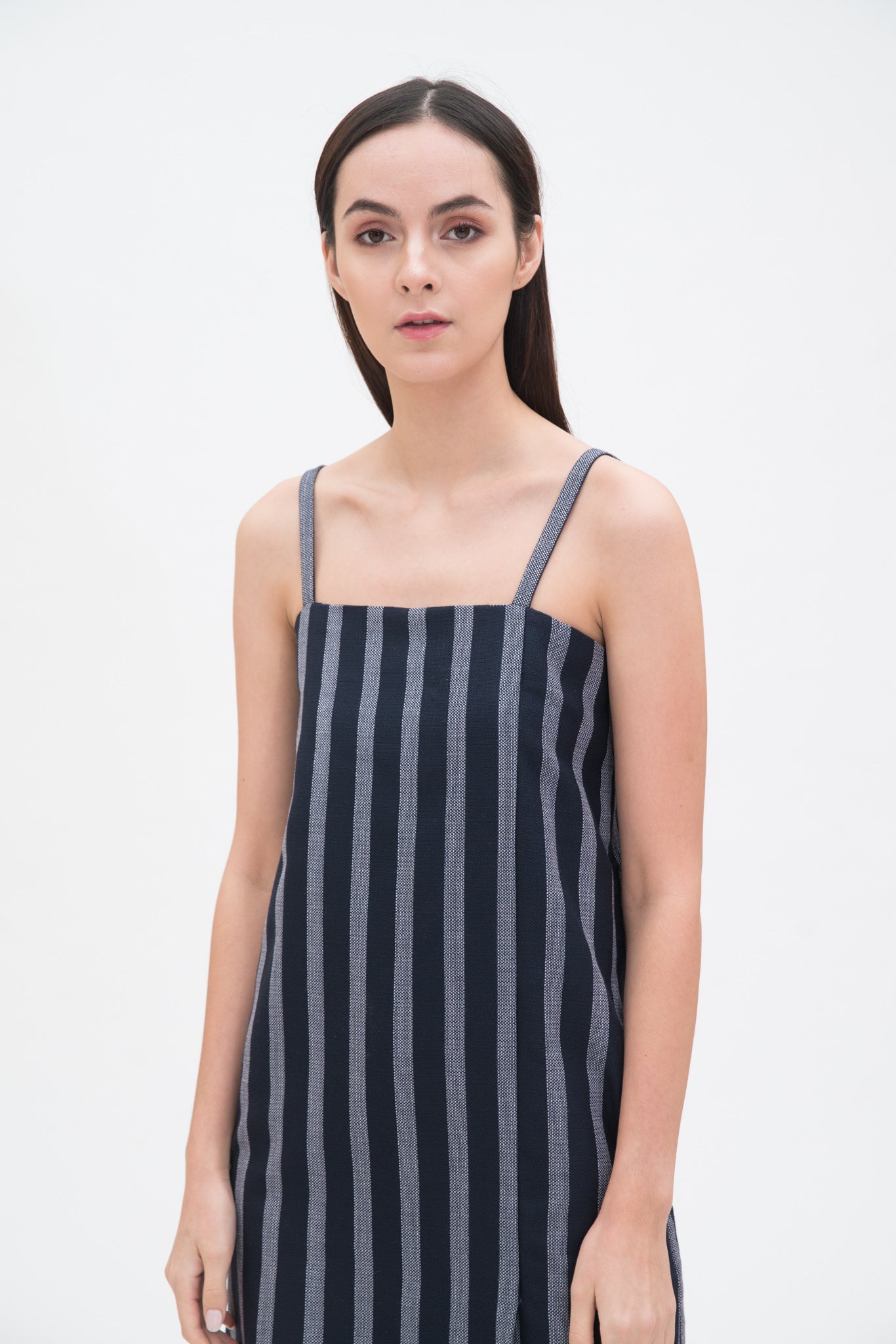 A woman with long brown hair is wearing a navy striped strappy dress.
