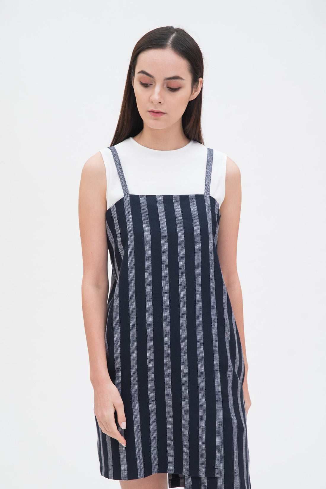 A woman with long brown hair is wearing a navy striped scrappy dress with a white top underneath.