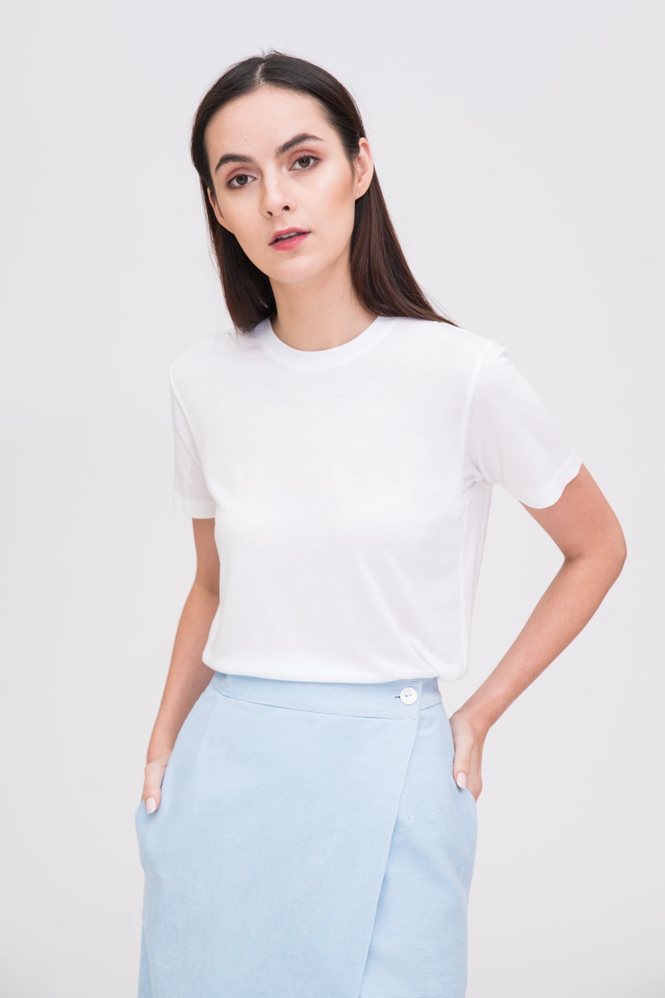 A woman with long dark hair is wearing a white t-shirt and light blue asymmetric skirt