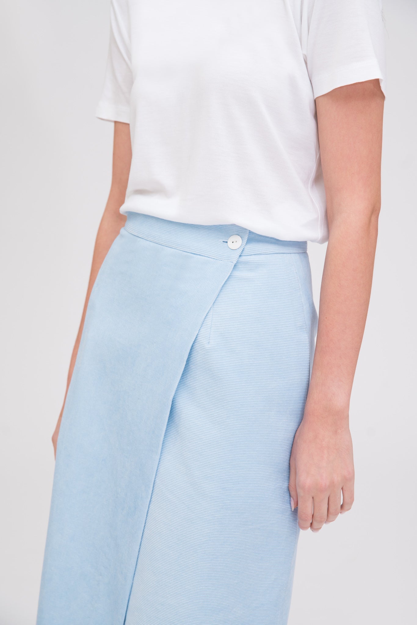 A woman with long dark hair is wearing a white t-shirt, light blue asymmetric skirt