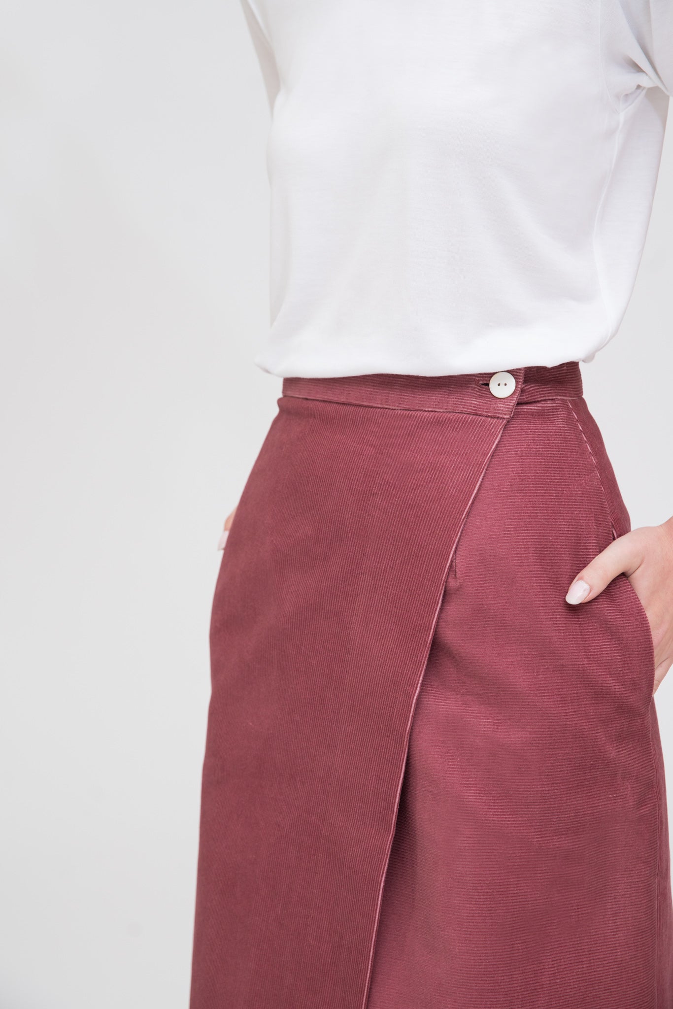 A woman with long dark hair is wearing a white t-shirt and dusty pink asymmetric skirt.