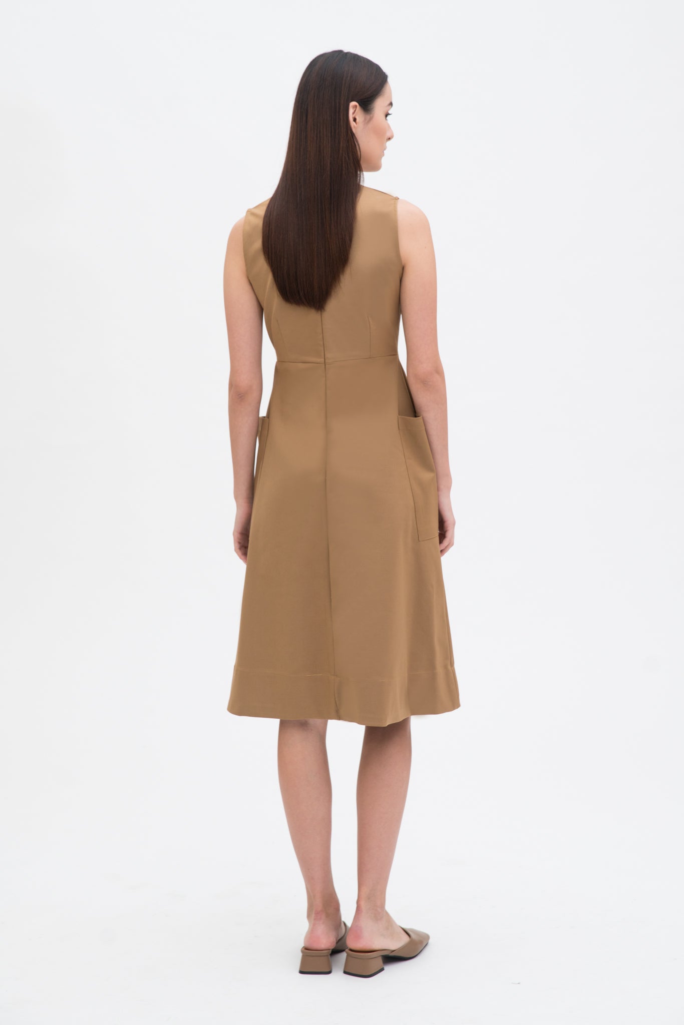 A woman with long dark hair is wearing a knee length camel dress with pockets. She is wearing camel leather shoes.