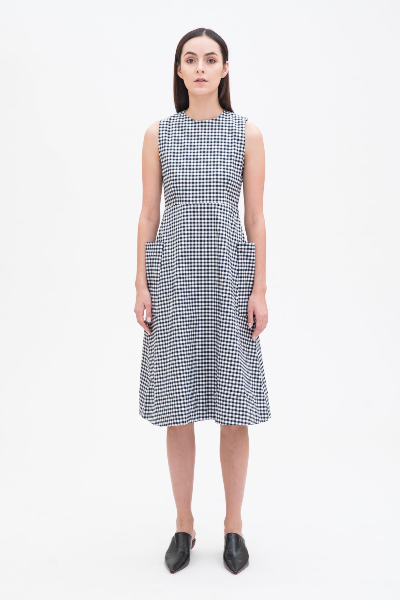 A woman with long dark hair is wearing a black and white checked dress. She has black leather shoes on.