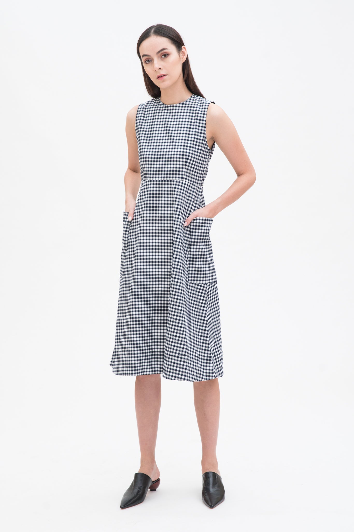 A woman with long dark hair is wearing a black and white checked dress. She has black leather shoes on.