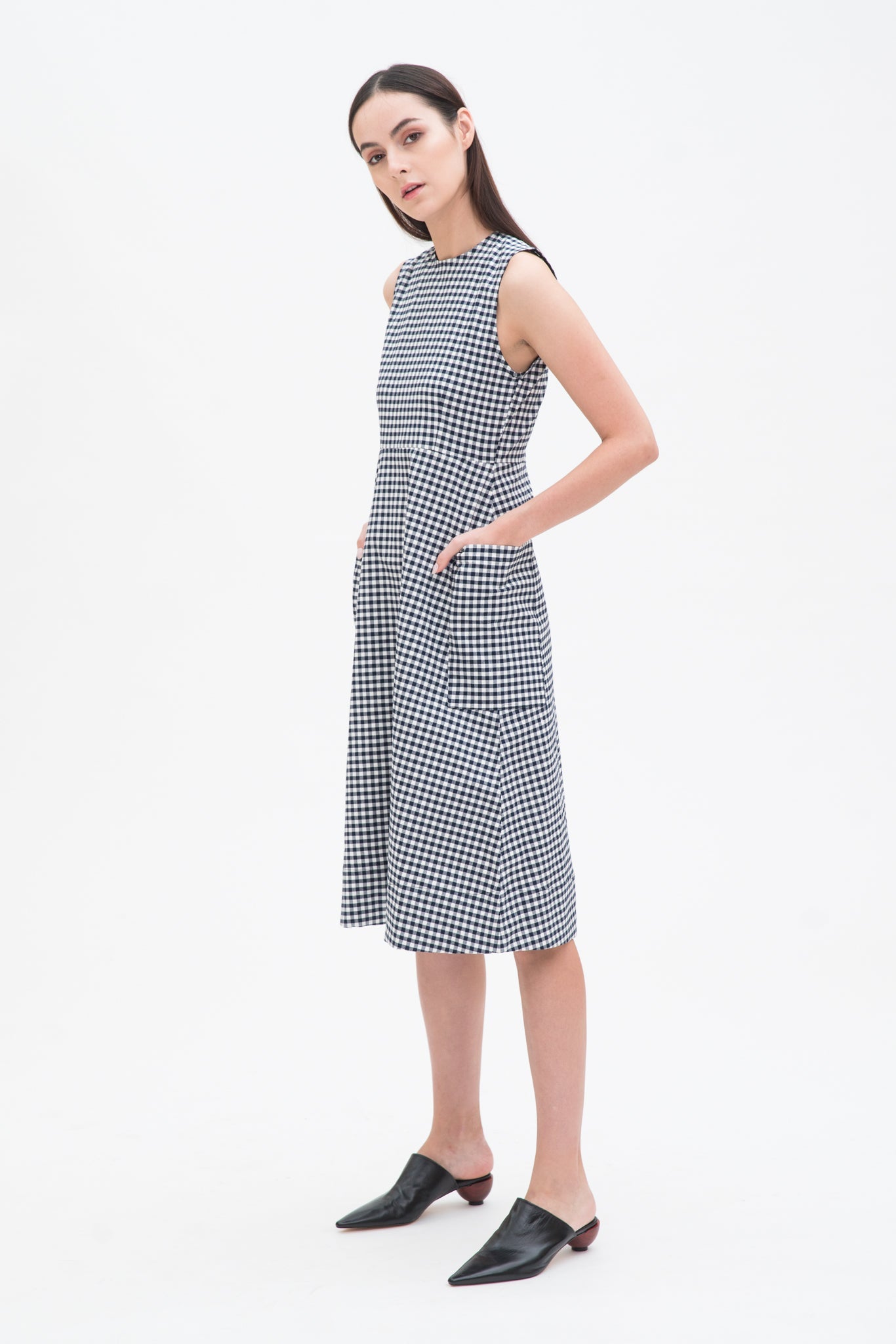 A woman with long dark hair is wearing a black and white checked dress. She has black leather shoes on.