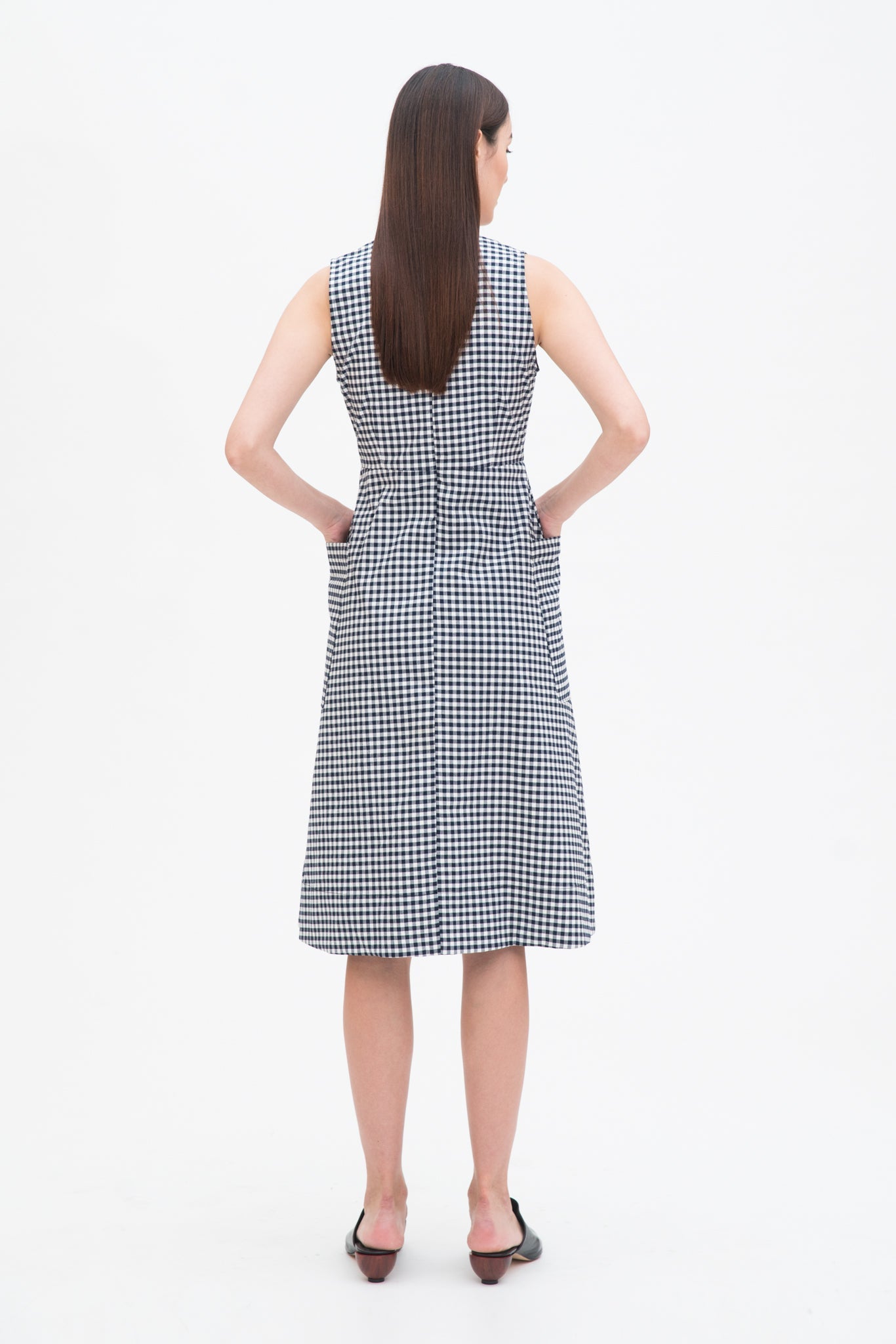 A woman with long dark hair is wearing a black and white checked dress. She has black leather shoes on.