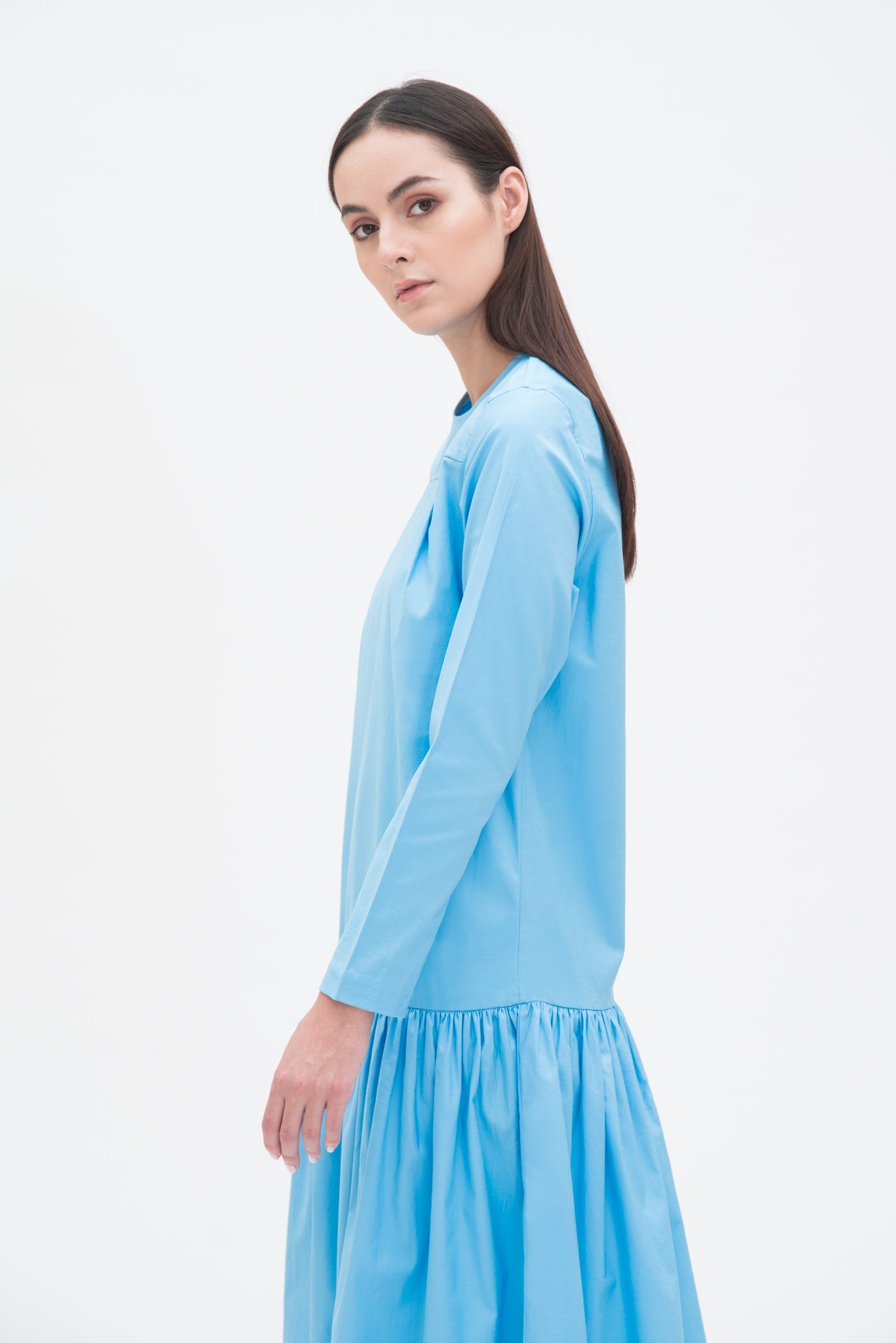 A woman with long brown hair is wearing a drop waist blue dress with ruffle hem.