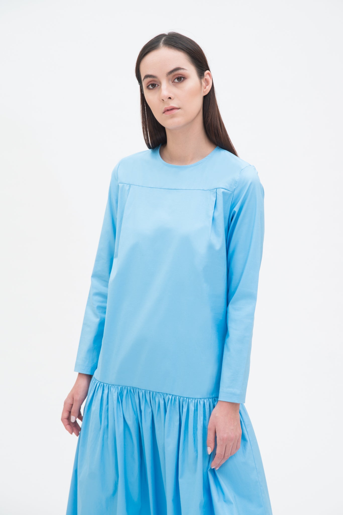A woman with long brown hair is wearing a drop waist blue dress with ruffle hem.