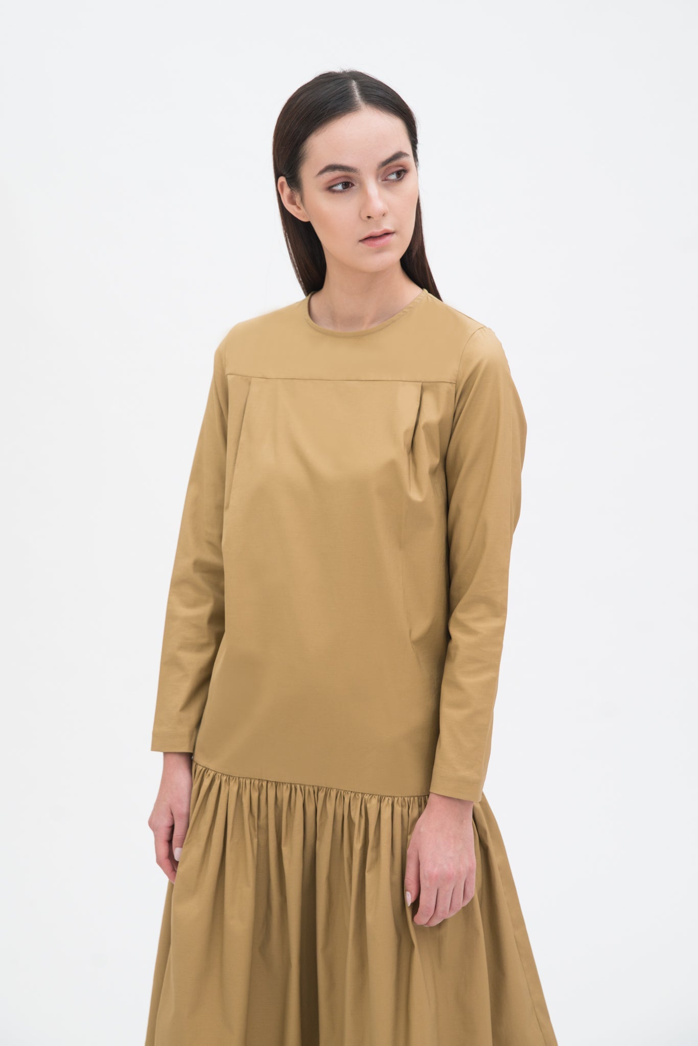 A woman with long brown hair is wearing a drop waist camel dress with ruffle hem.