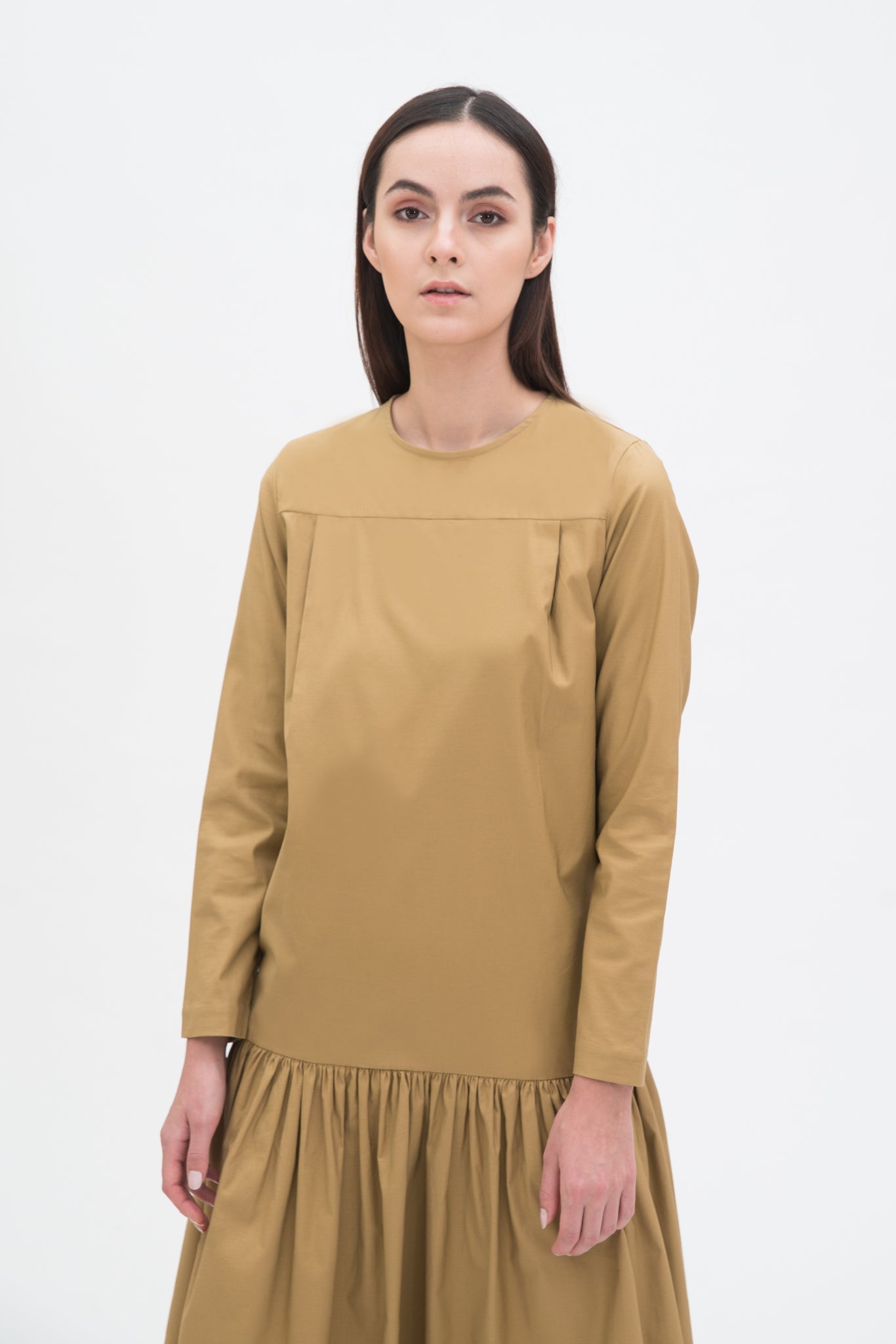 A woman with long brown hair is wearing a drop waist camel dress with ruffle hem.
