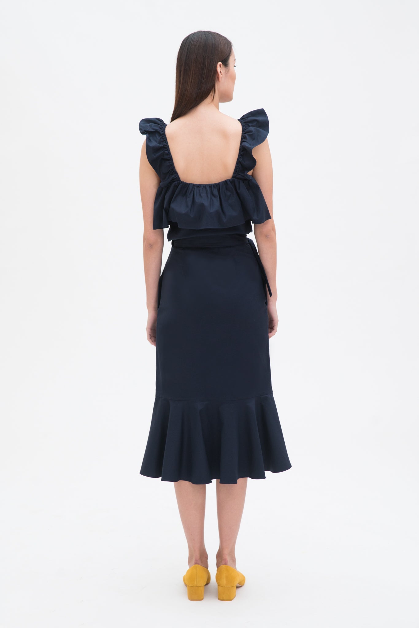 A woman is wearing a navy ruffled top and skirt. She is also wearing yellow shoes.