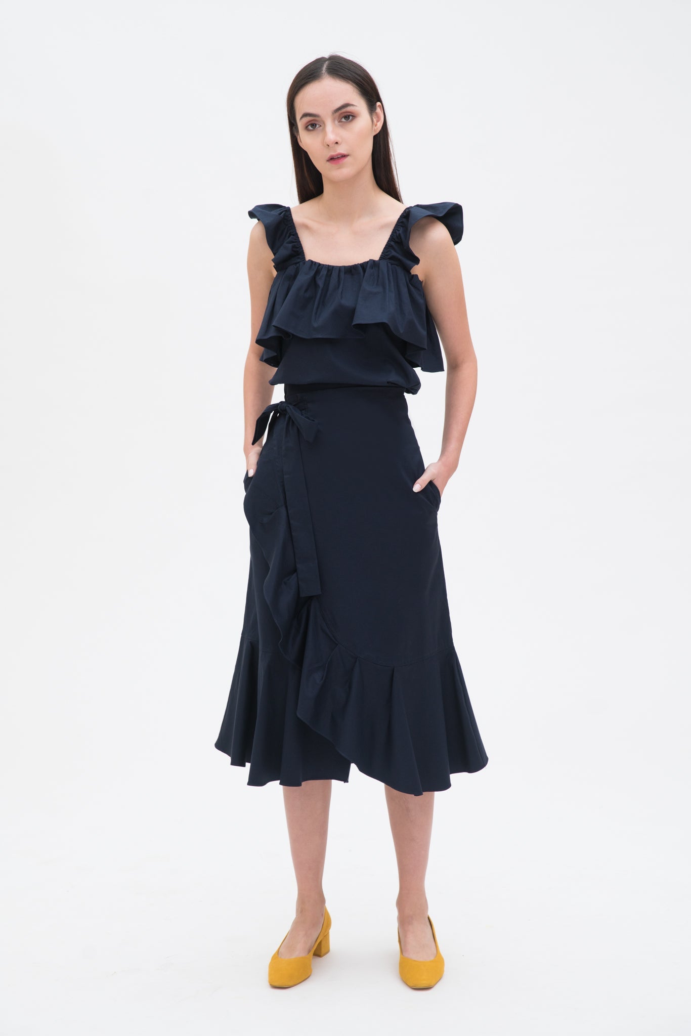 A woman is wearing a navy ruffled top and skirt. She is also wearing yellow shoes.