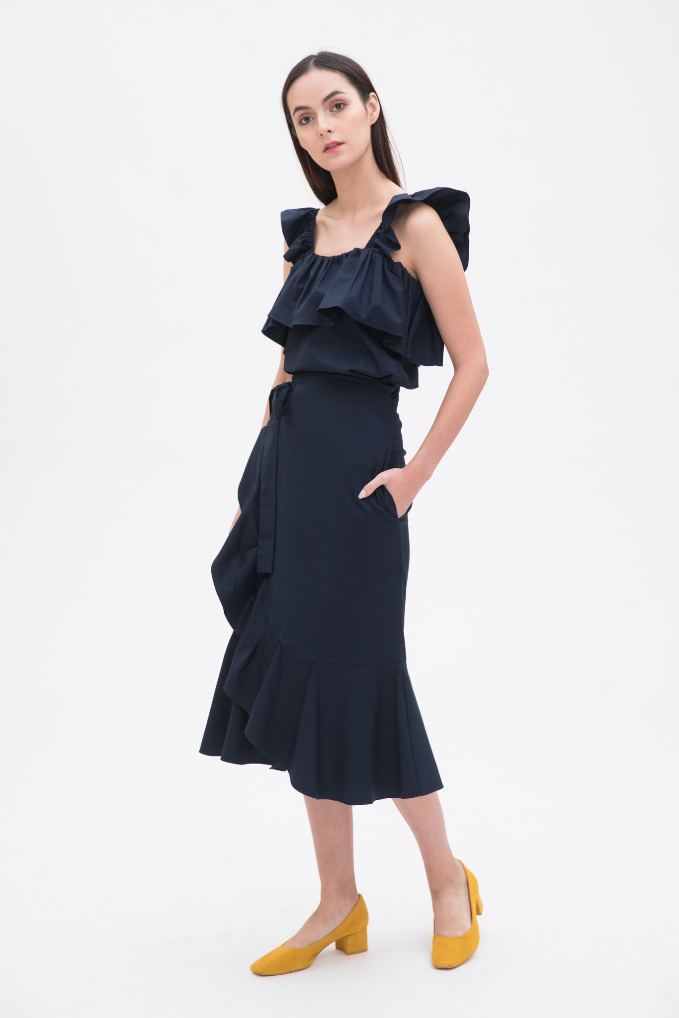 A woman is wearing a navy ruffled top and skirt. She is also wearing yellow shoes.