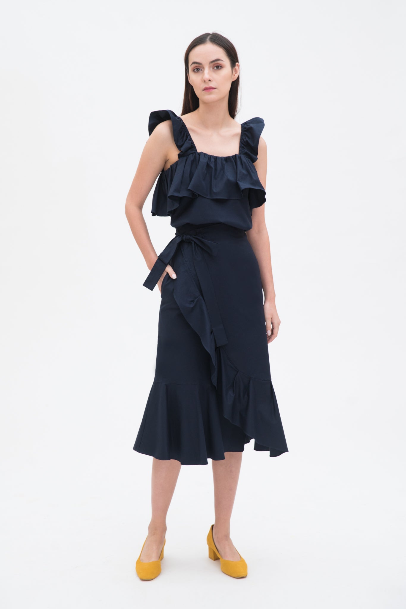 A woman is wearing a navy ruffled top and skirt. She is also wearing yellow shoes.