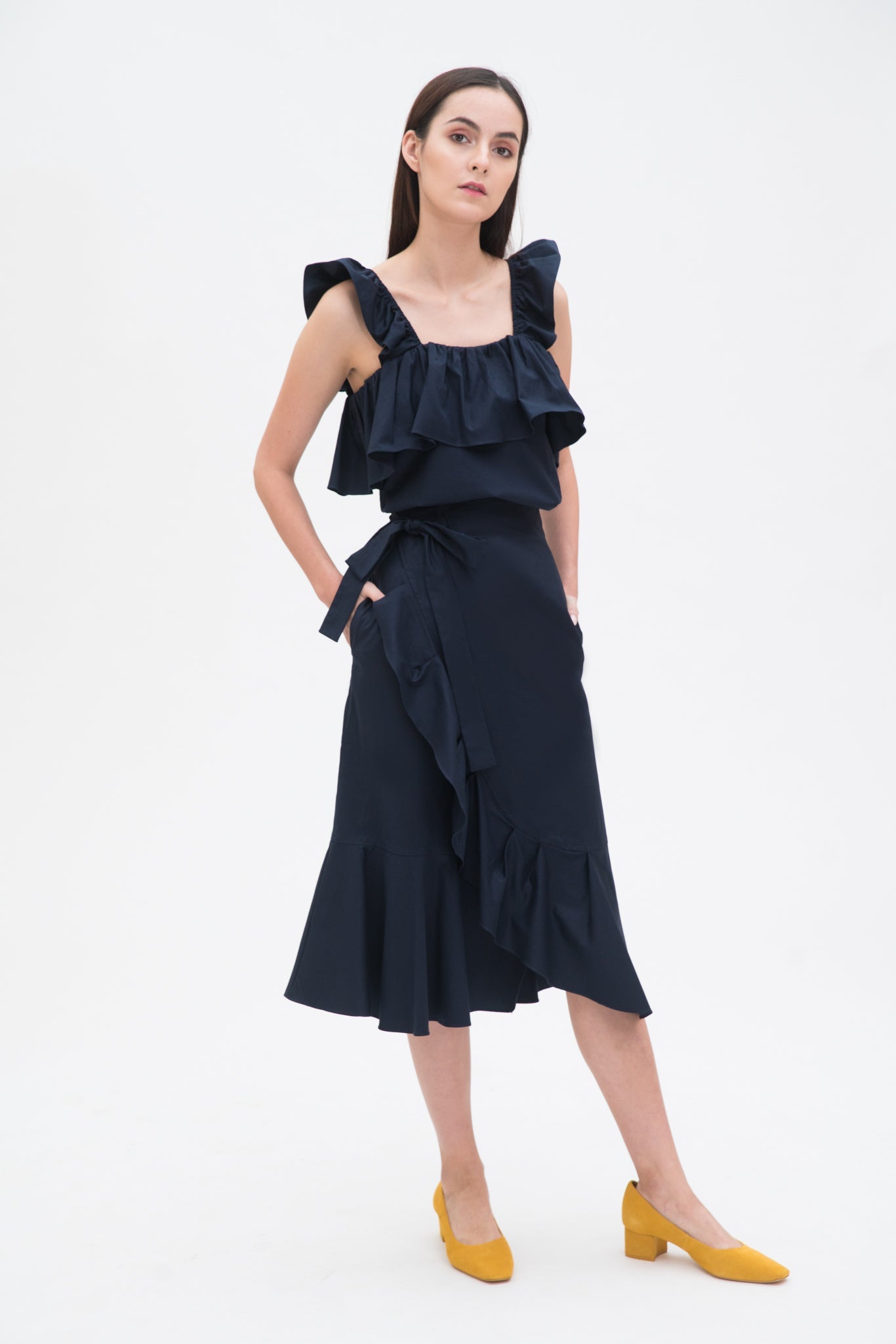 A woman is wearing a navy ruffled top and skirt. She is also wearing yellow shoes.