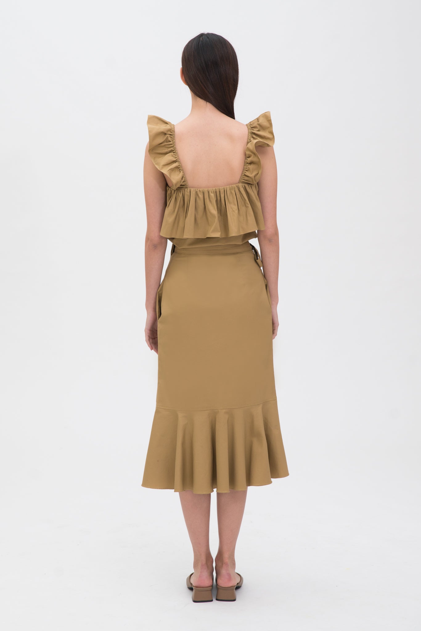 A woman is wearing a beige ruffled top and skirt. She is also wearing brown shoes.