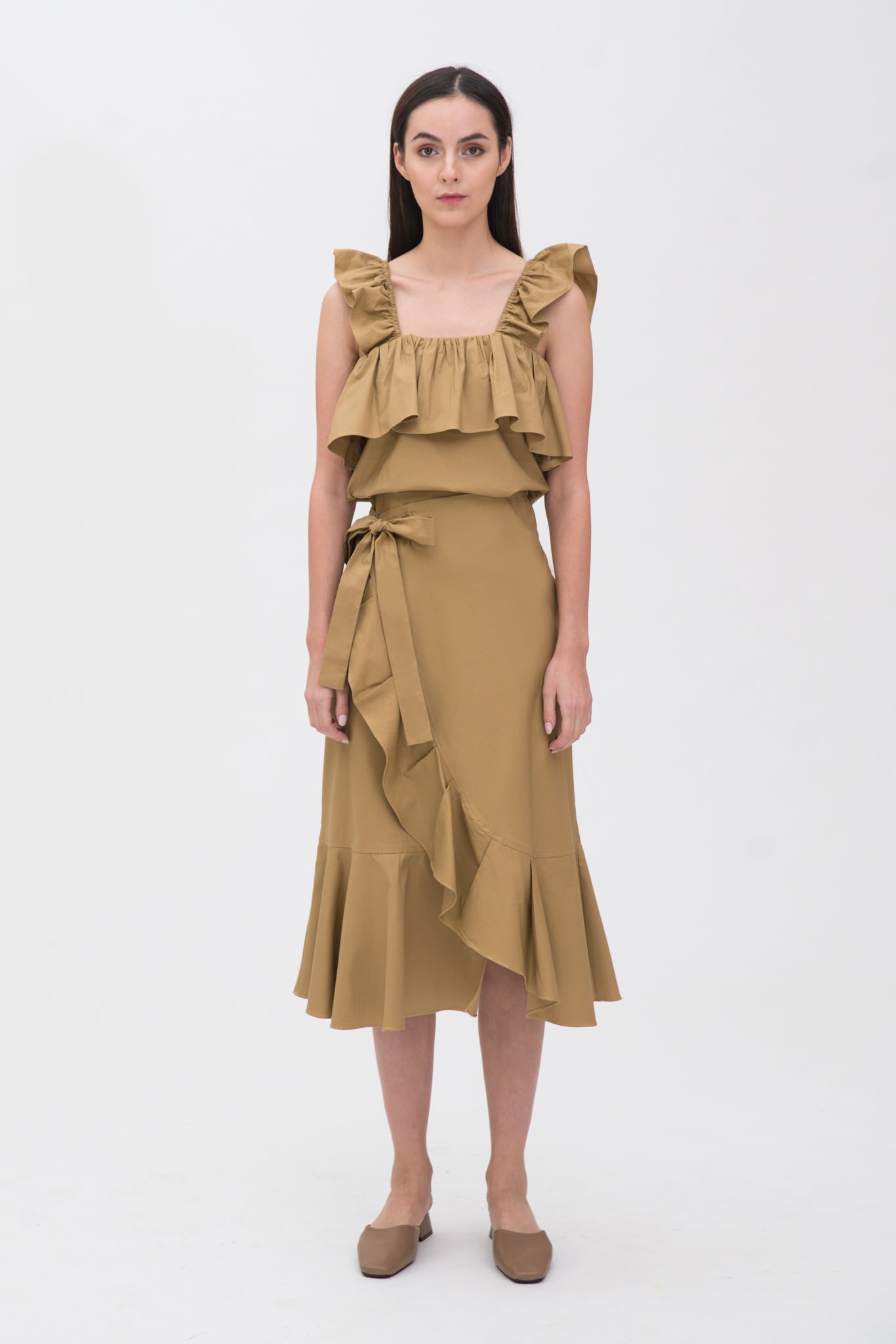 A woman is wearing a beige ruffled top and skirt. She is also wearing brown shoes.