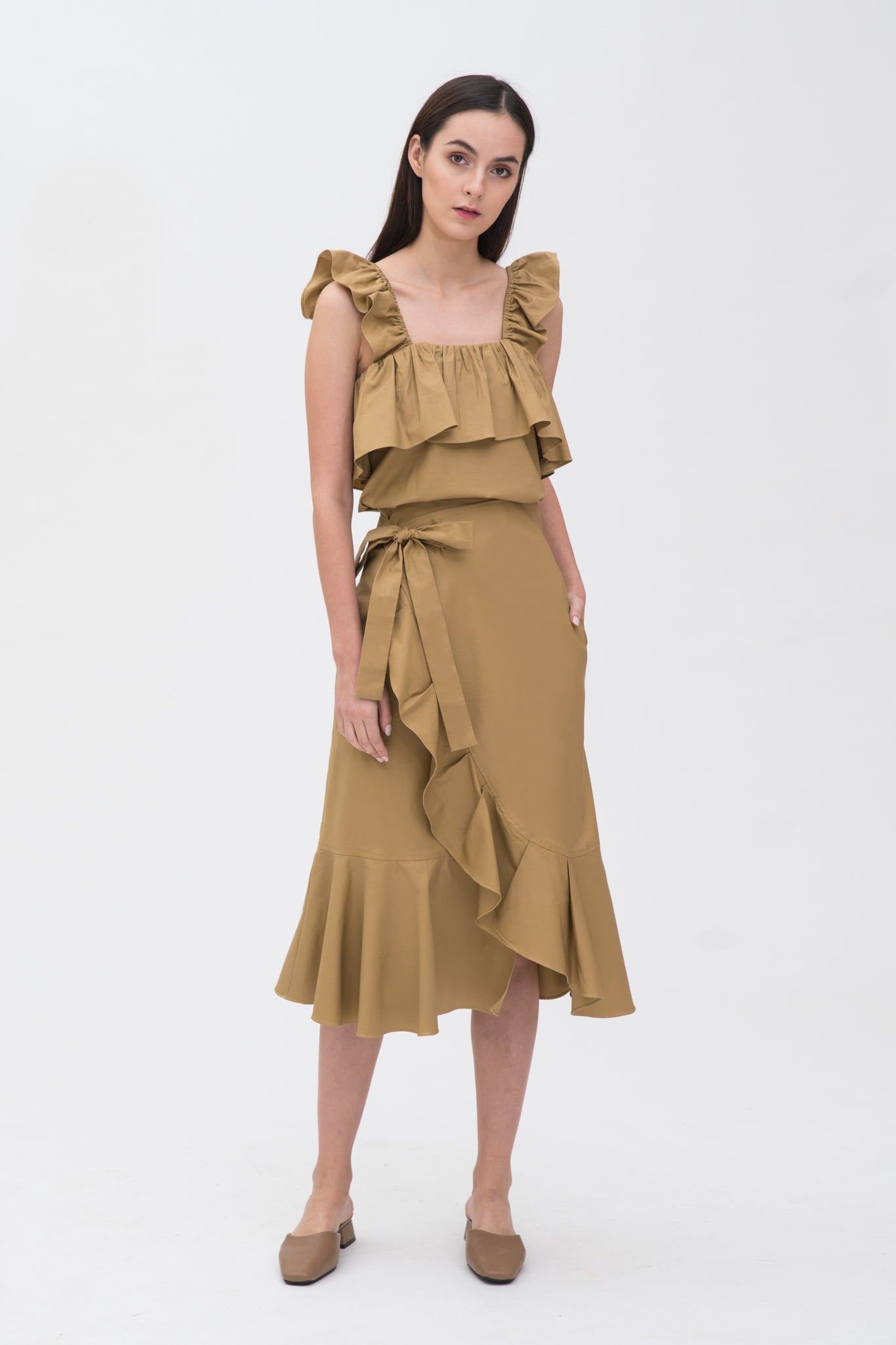 A woman is wearing a beige ruffled top and skirt. She is also wearing brown shoes.