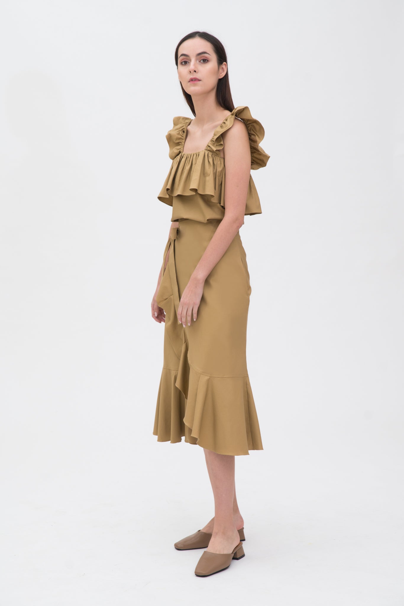 A woman is wearing a beige ruffled top and skirt. She is also wearing brown shoes.