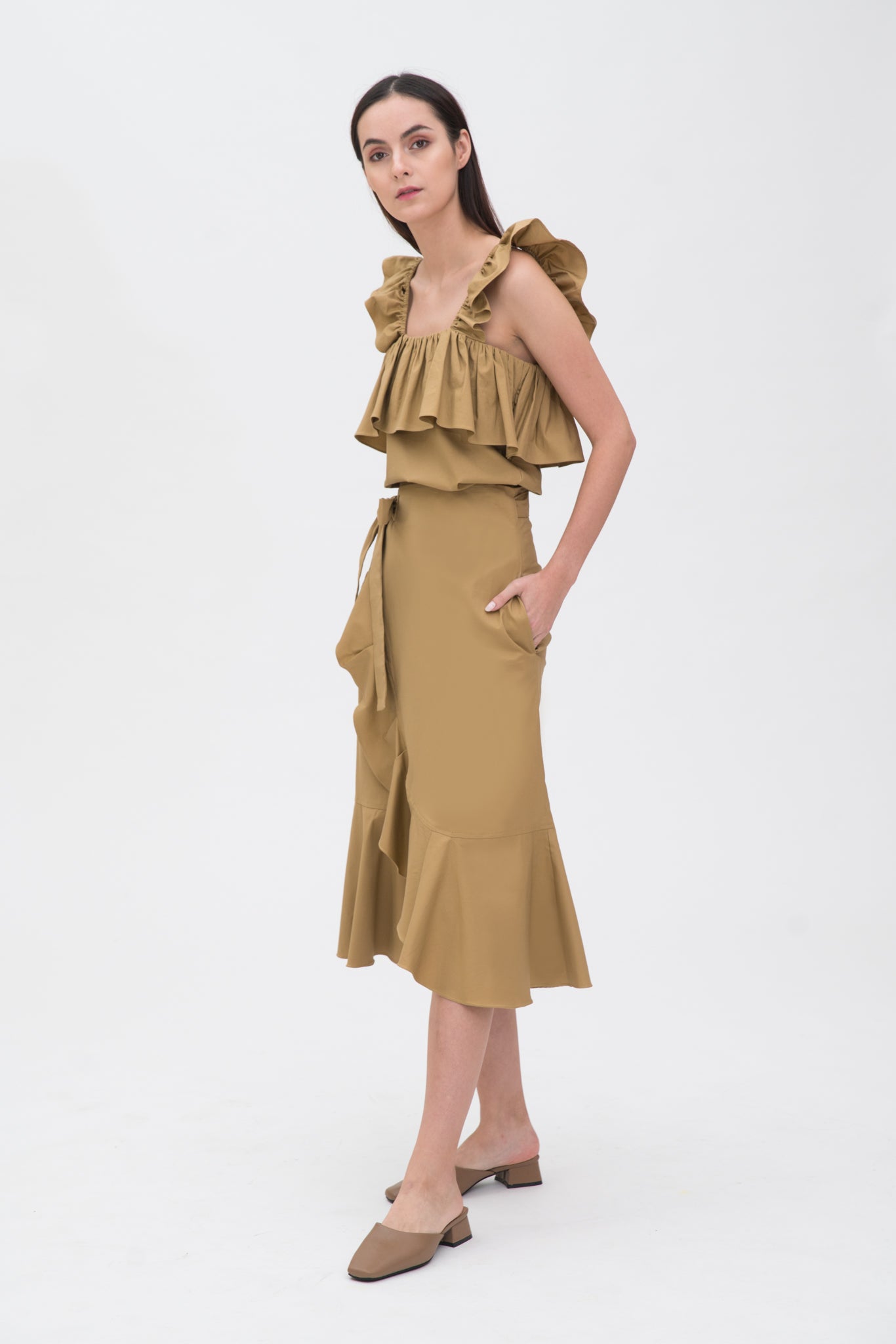 A woman is wearing a beige ruffled top and skirt. She is also wearing brown shoes.