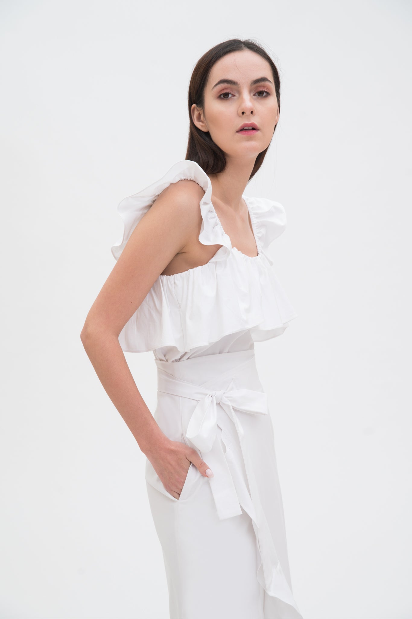 A woman is wearing a white ruffled scrappy dress.