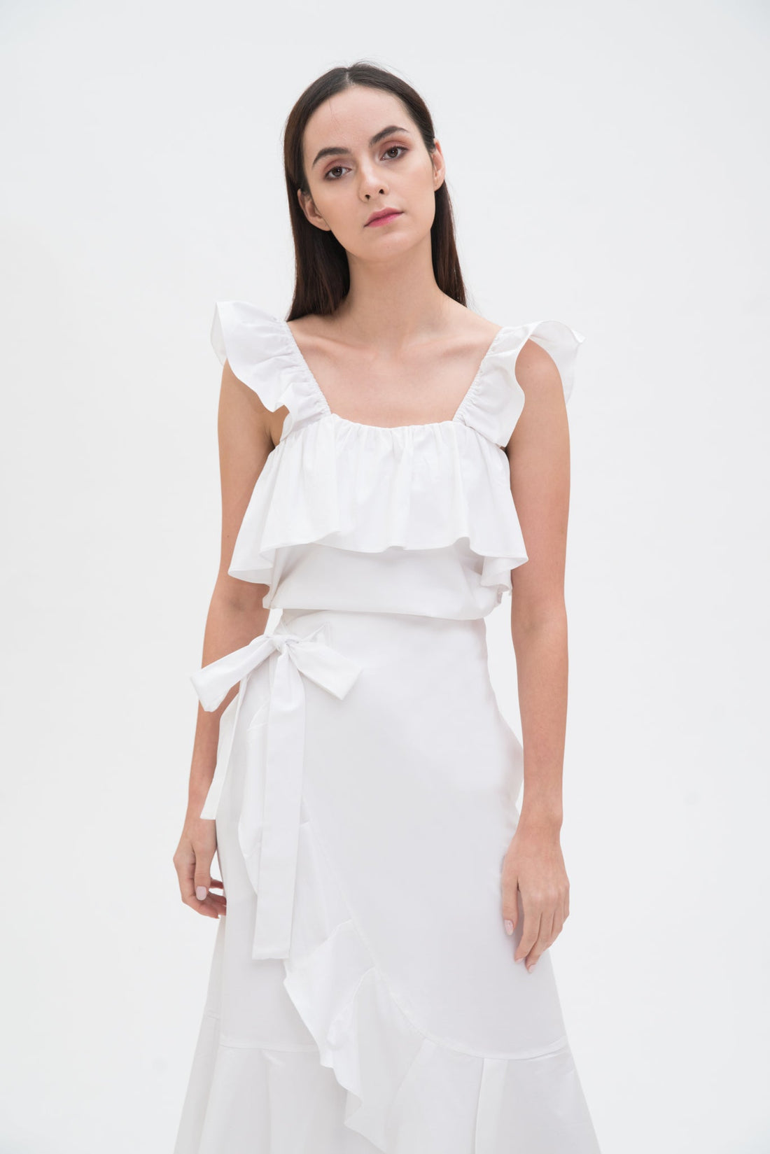 A woman is wearing a white ruffled scrappy dress.