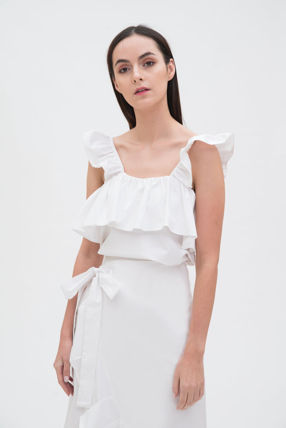 A woman is wearing a white ruffled scrappy dress.