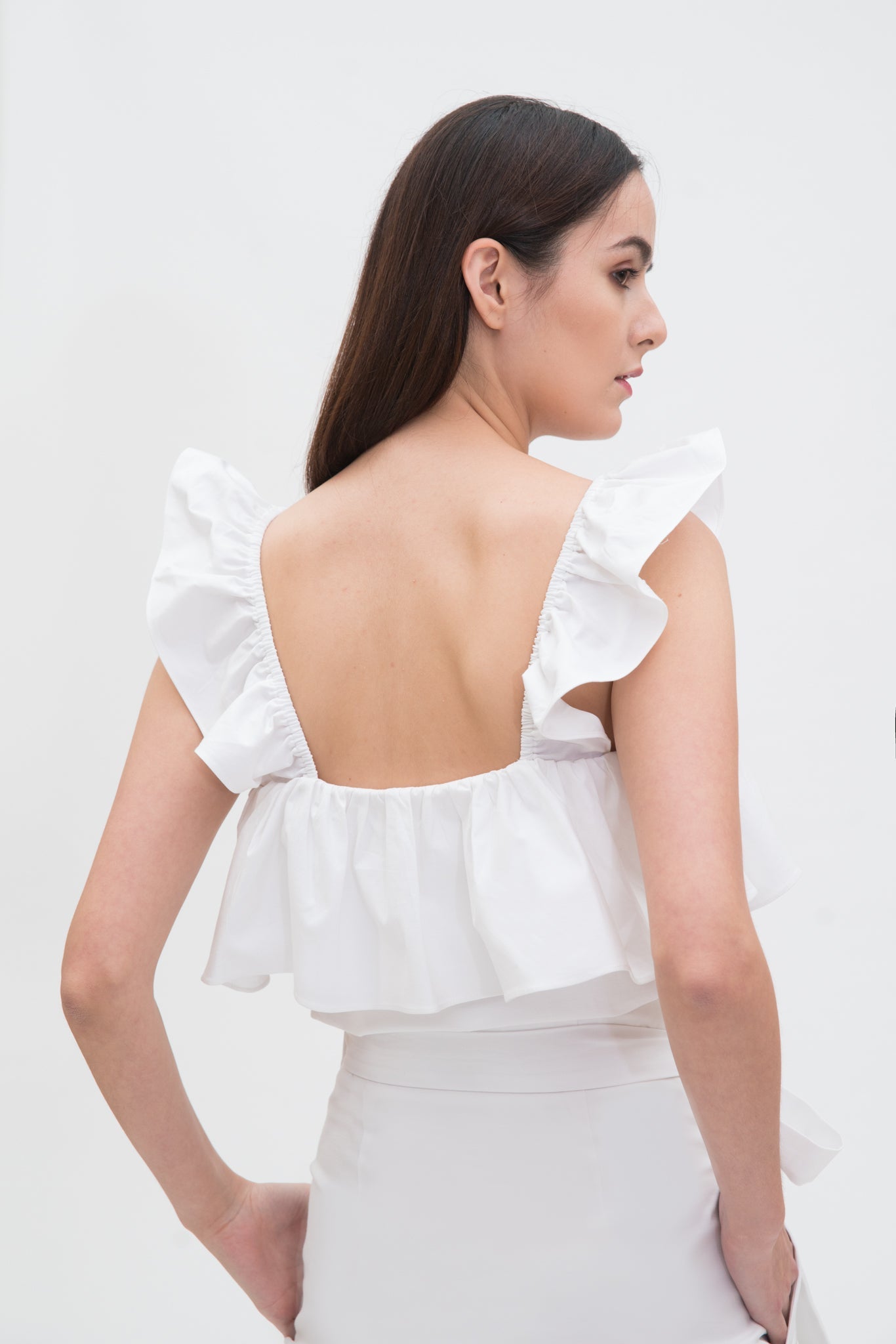 A woman is wearing a white ruffled scrappy dress.