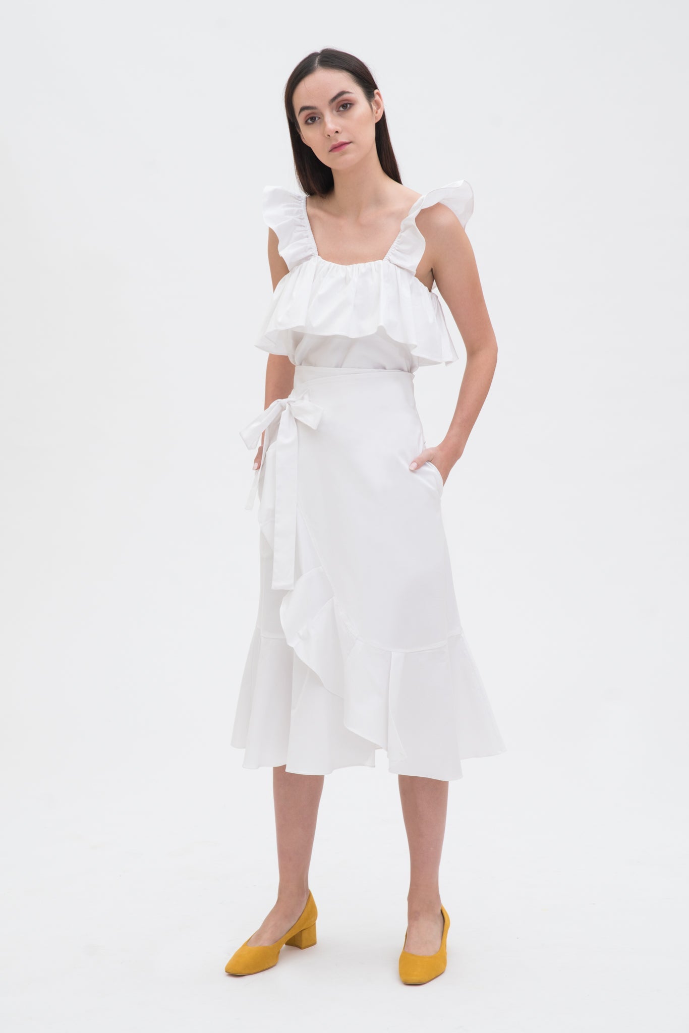 A woman is wearing a white ruffled top and skirt. She is also wearing yellow shoes.
