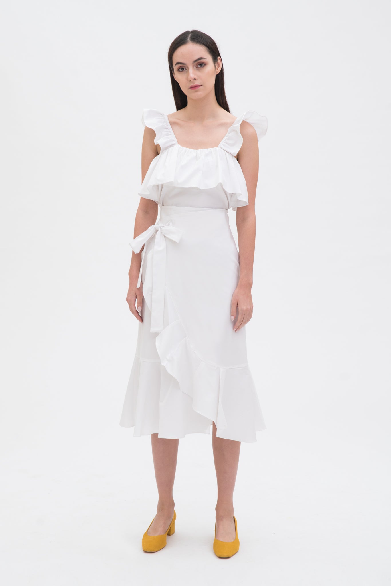 A woman is wearing a white ruffled scrappy dress.