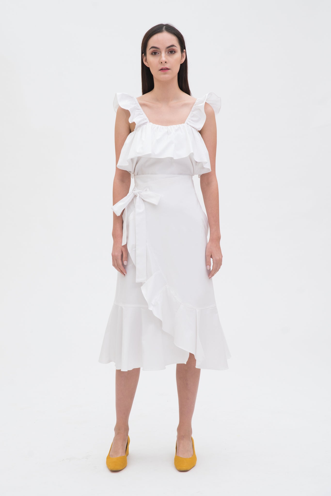 A woman is wearing a white ruffled scrappy dress.