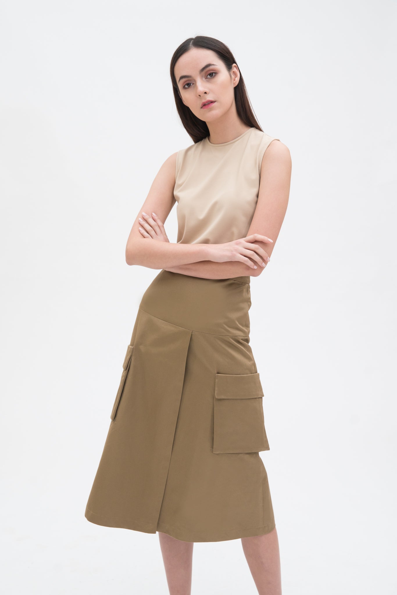 A woman with long dark hair is wearing a beige tank top and a knee length camel skirt with large pockets.