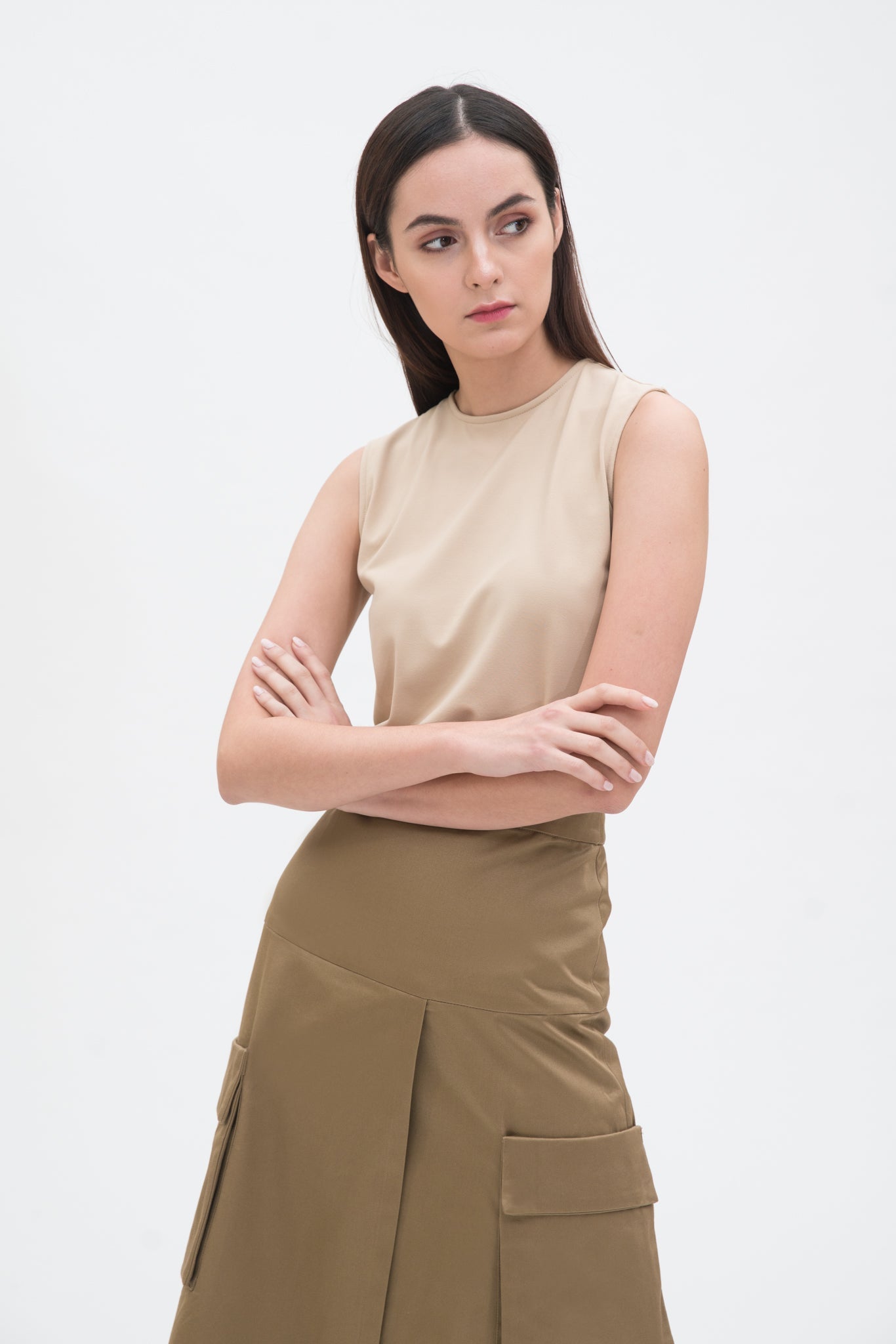 A woman with long dark hair is wearing a beige tank top and a knee length camel skirt with large pockets.