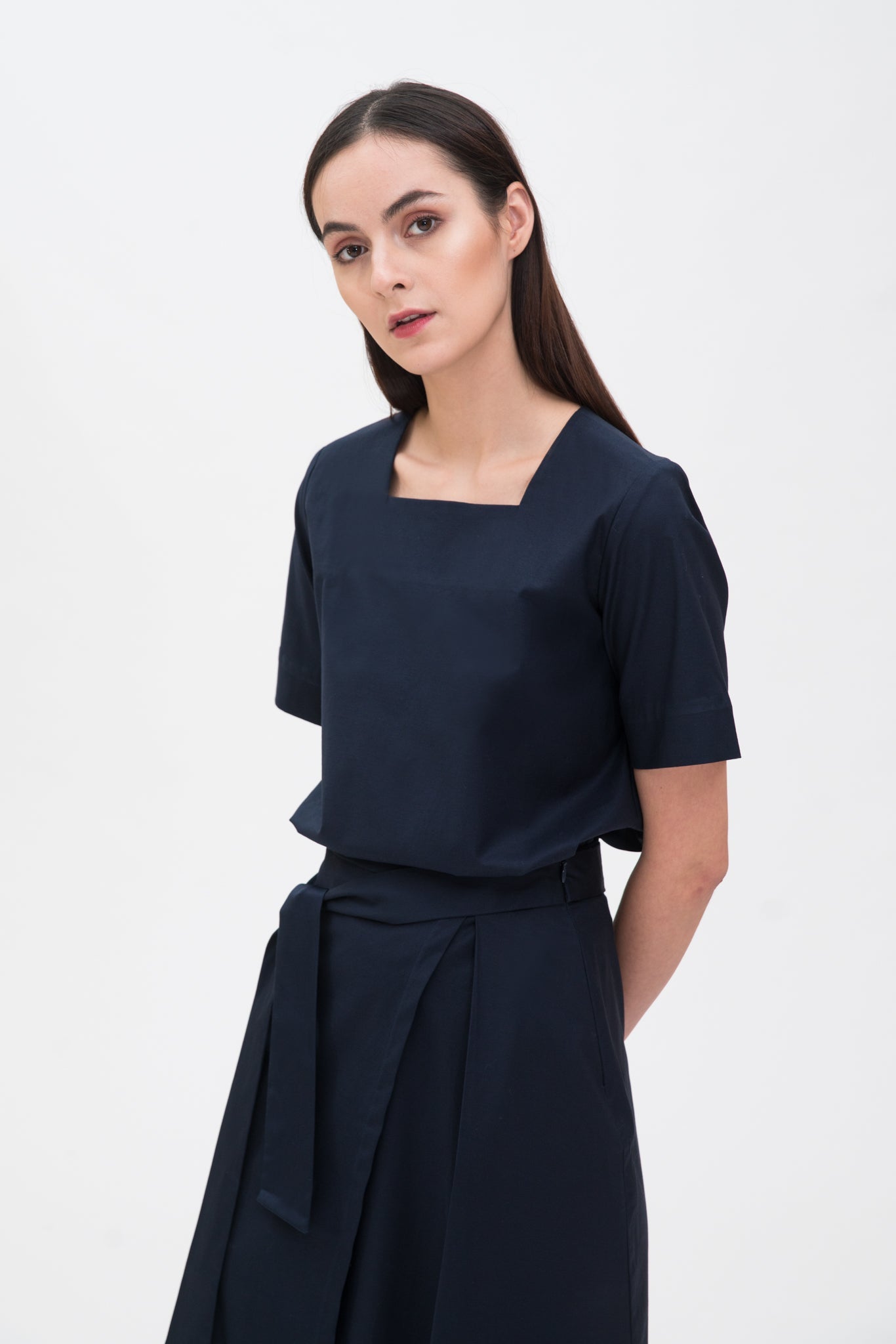 A woman with long dark hair is wearing a navy t-shirt and asymmetric navy skirt