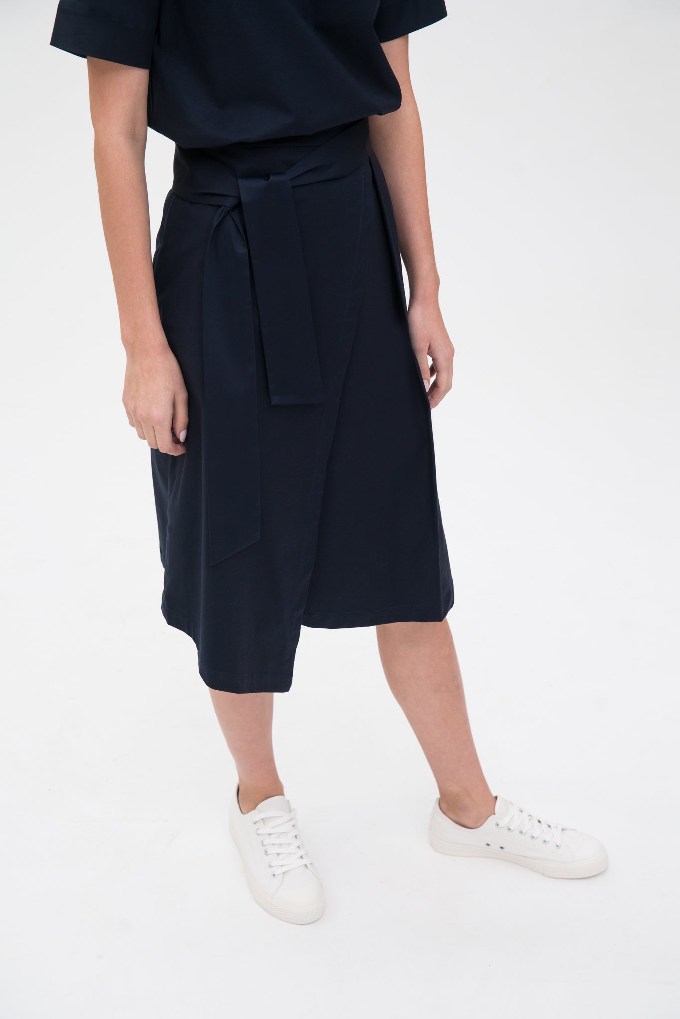 A woman is wearing a navy t-shirt and asymmetric navy skirt  with white shoes