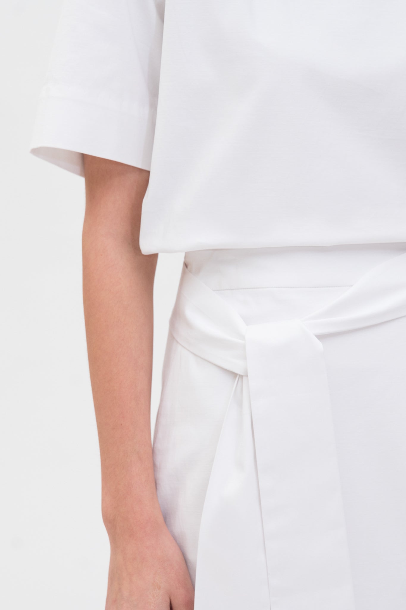 A woman is wearing a navy t-shirt and asymmetric white skirt  with white shoes