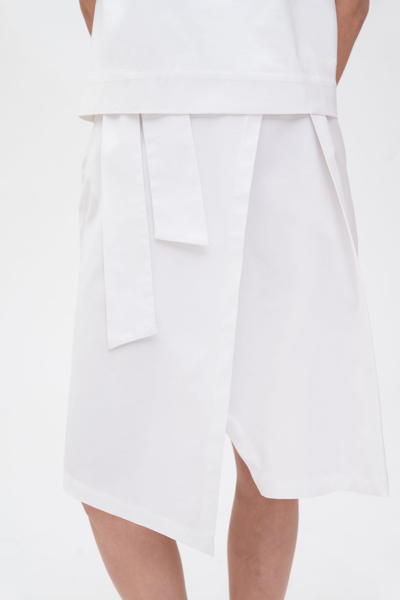 A woman is wearing a navy t-shirt and asymmetric white skirt  with white shoes