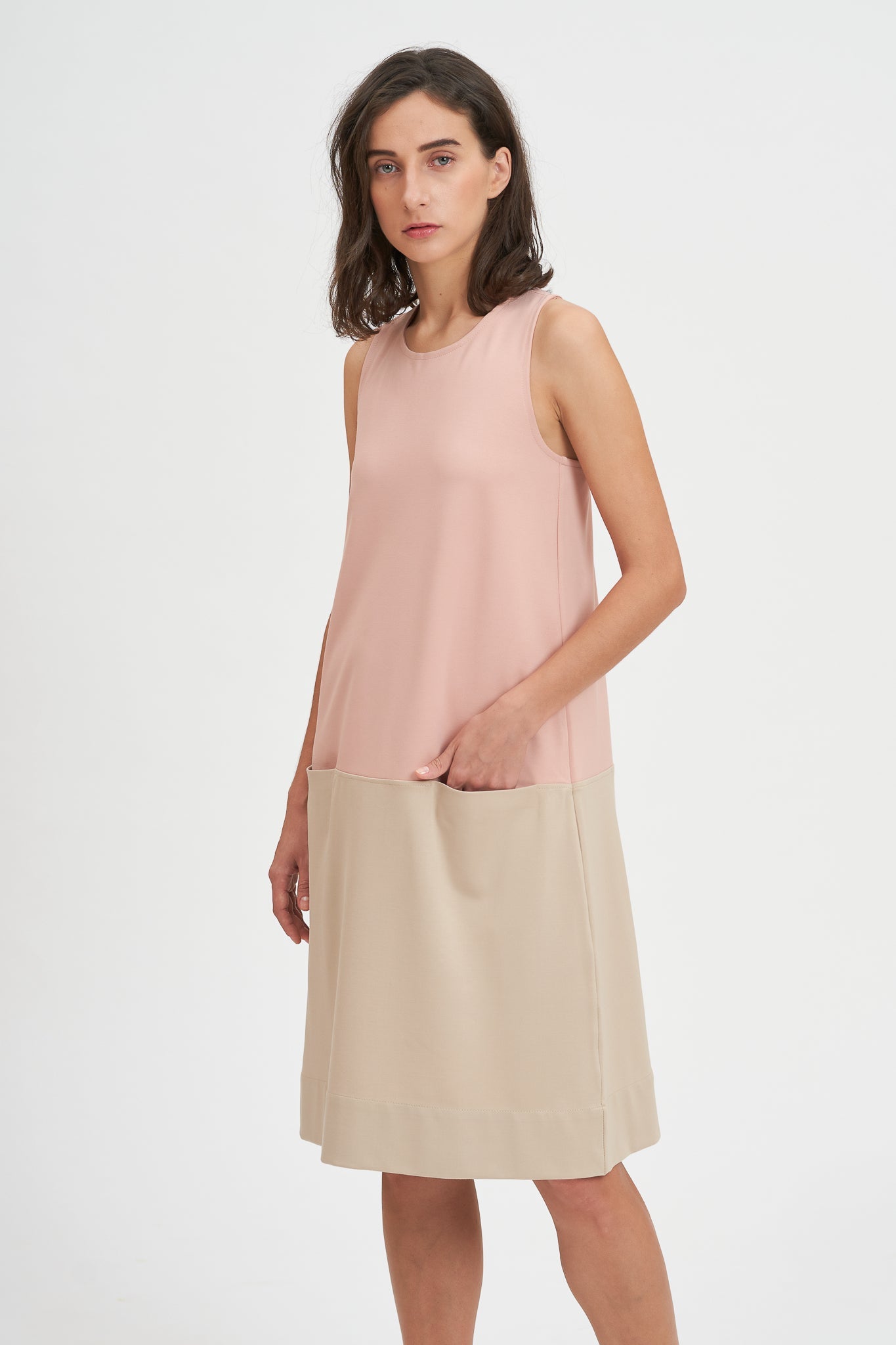A woman with shoulder length brown hair is wearing a pale pink and nude knee length dress. She also has white tennis shoes on.