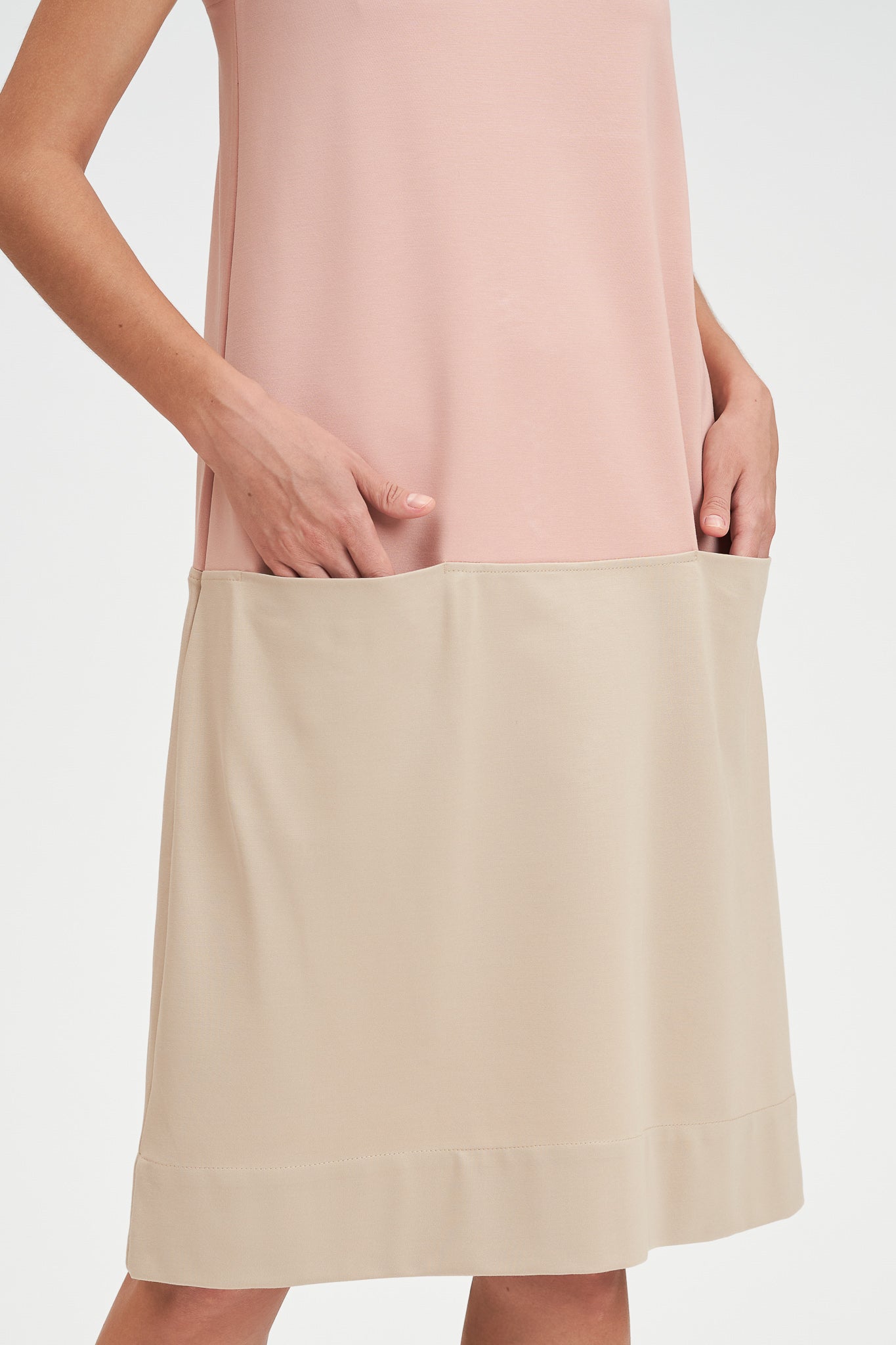 A woman with shoulder length brown hair is wearing a pale pink and nude knee length dress.