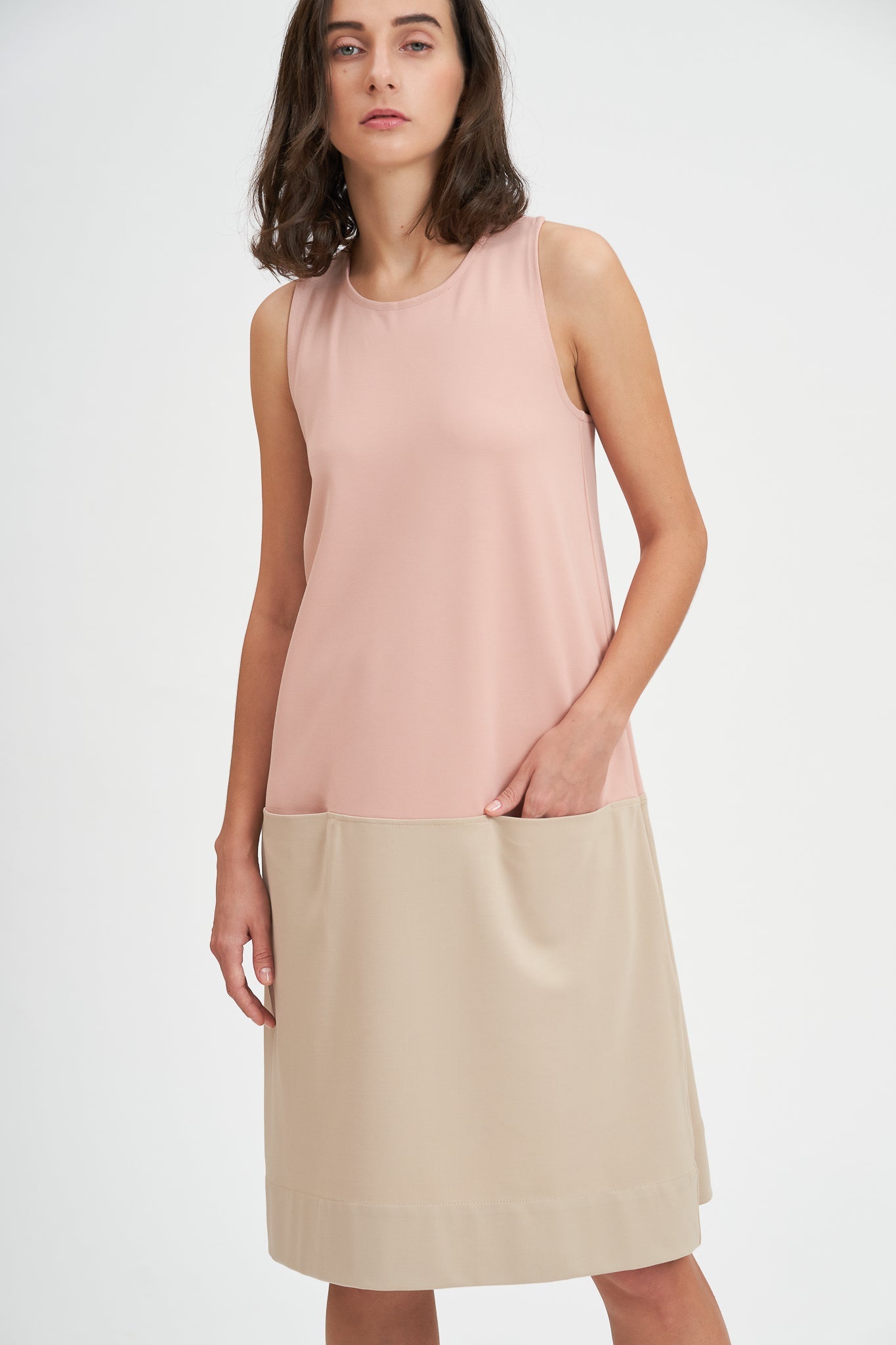 A woman with shoulder length brown hair is wearing a pale pink and nude knee length dress.
