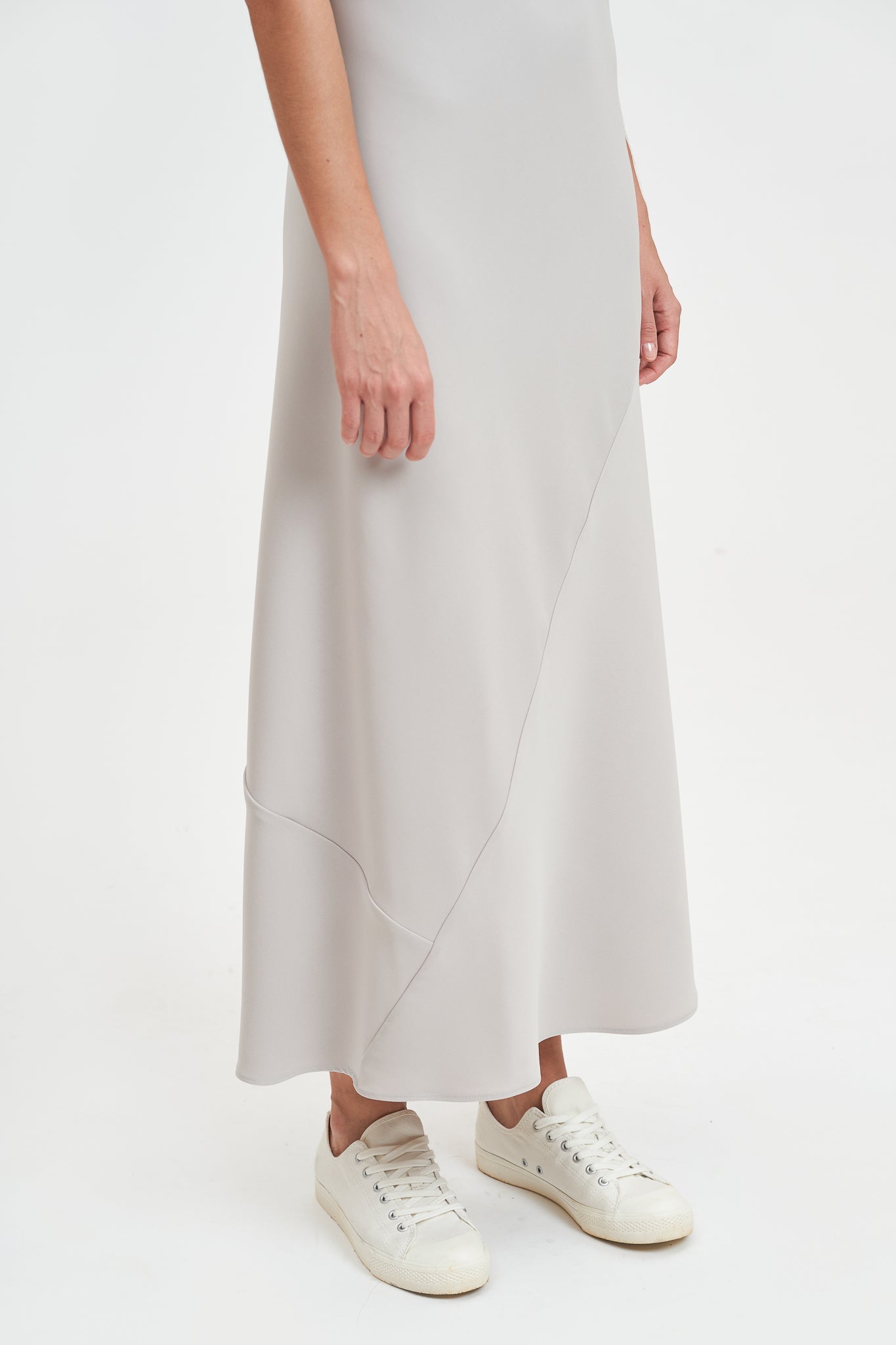 A woman with shoulder length hair is wearing an ankle length gray strappy dress. She is wearing white tennis shoes.