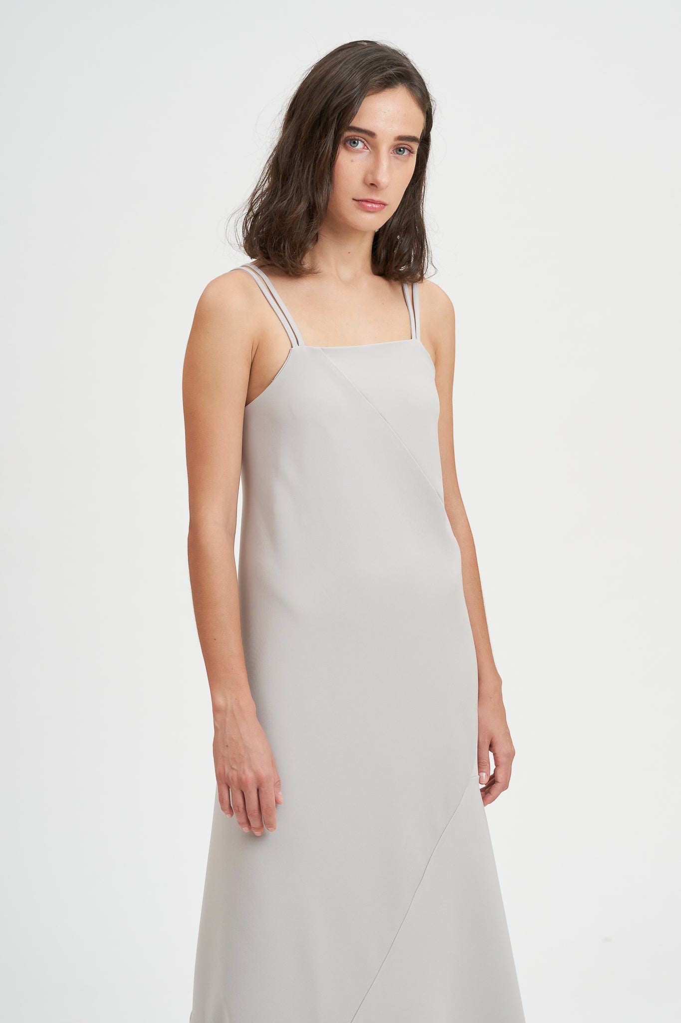 A woman with shoulder length hair is wearing an ankle length gray strappy dress.