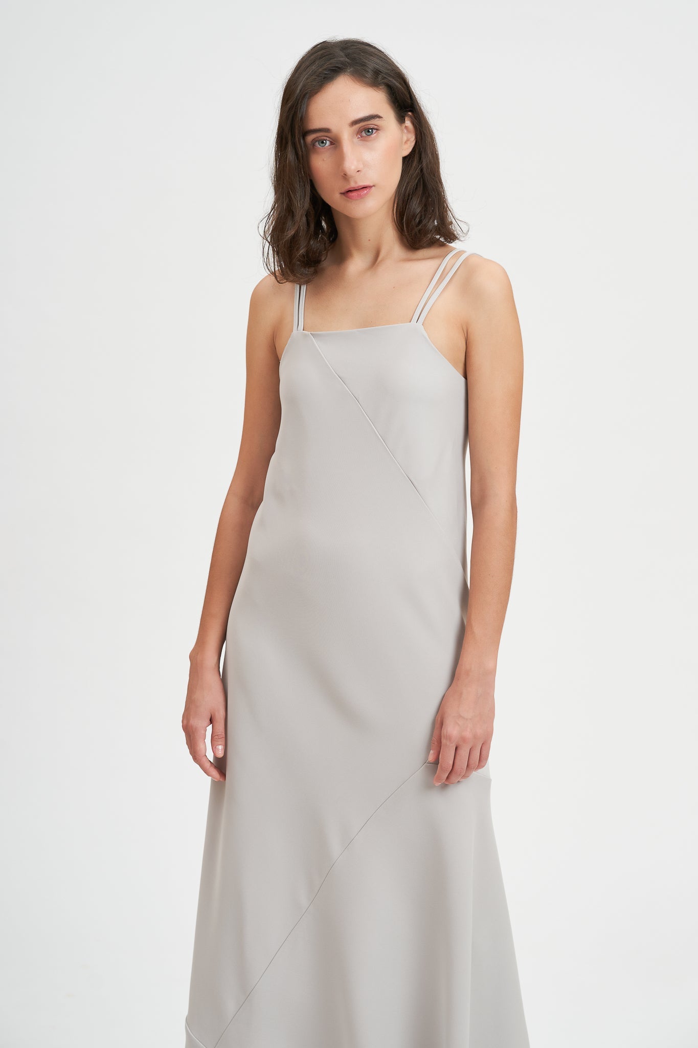 A woman with shoulder length hair is wearing an ankle length gray strappy dress.